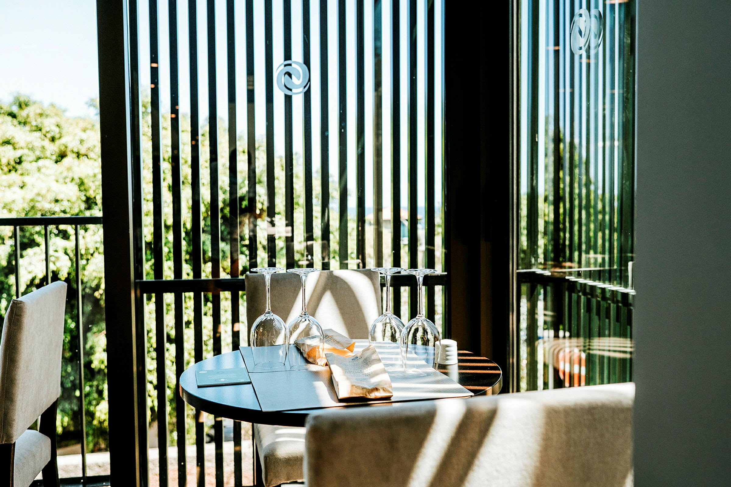 Et dekket bord med glass på en terrasse med grønne trær i bakgrunnen. (AI-generert tekst)