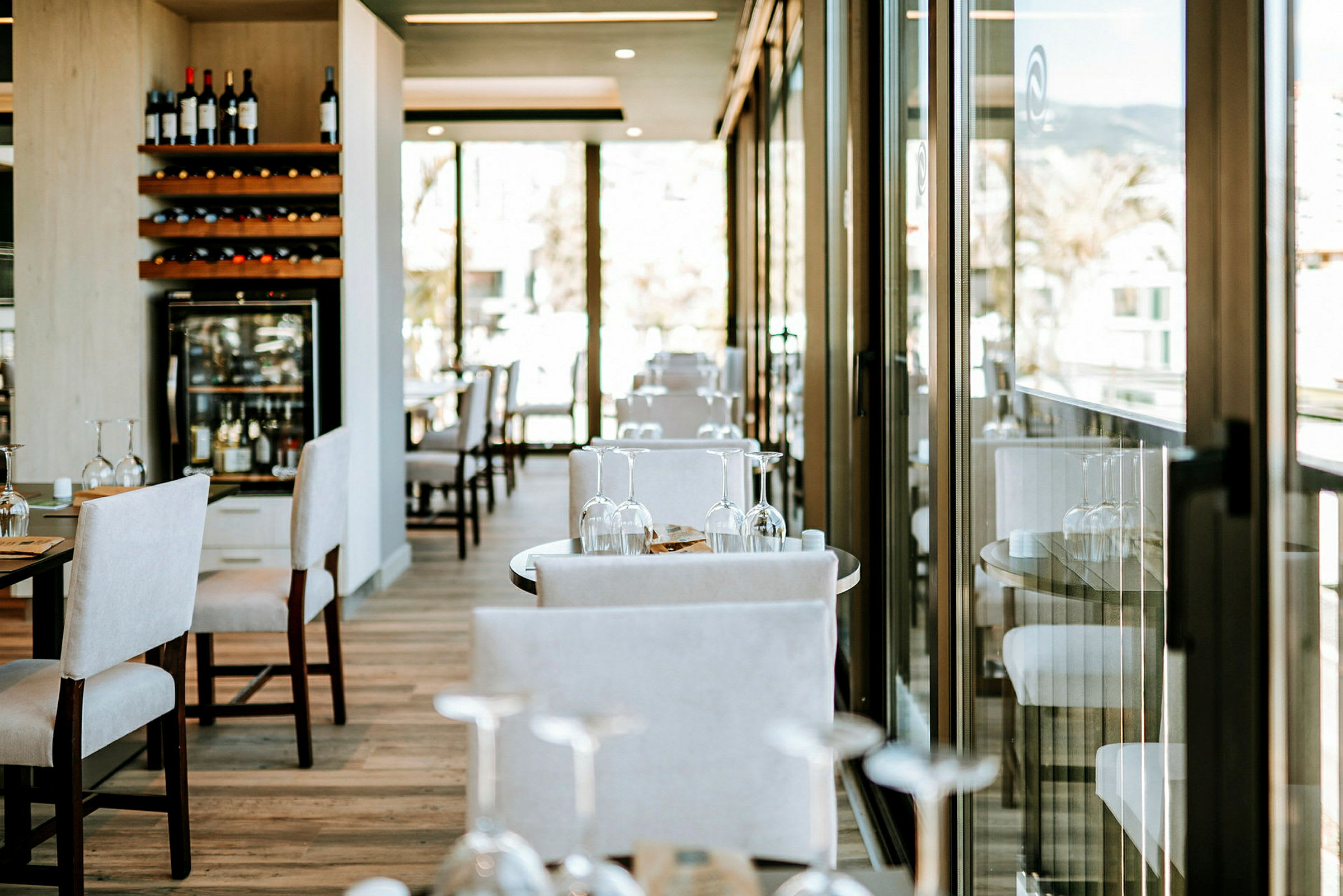 En restaurant med bord og stoler samt glassdører som slipper inn naturlig lys. (AI-generert tekst)
