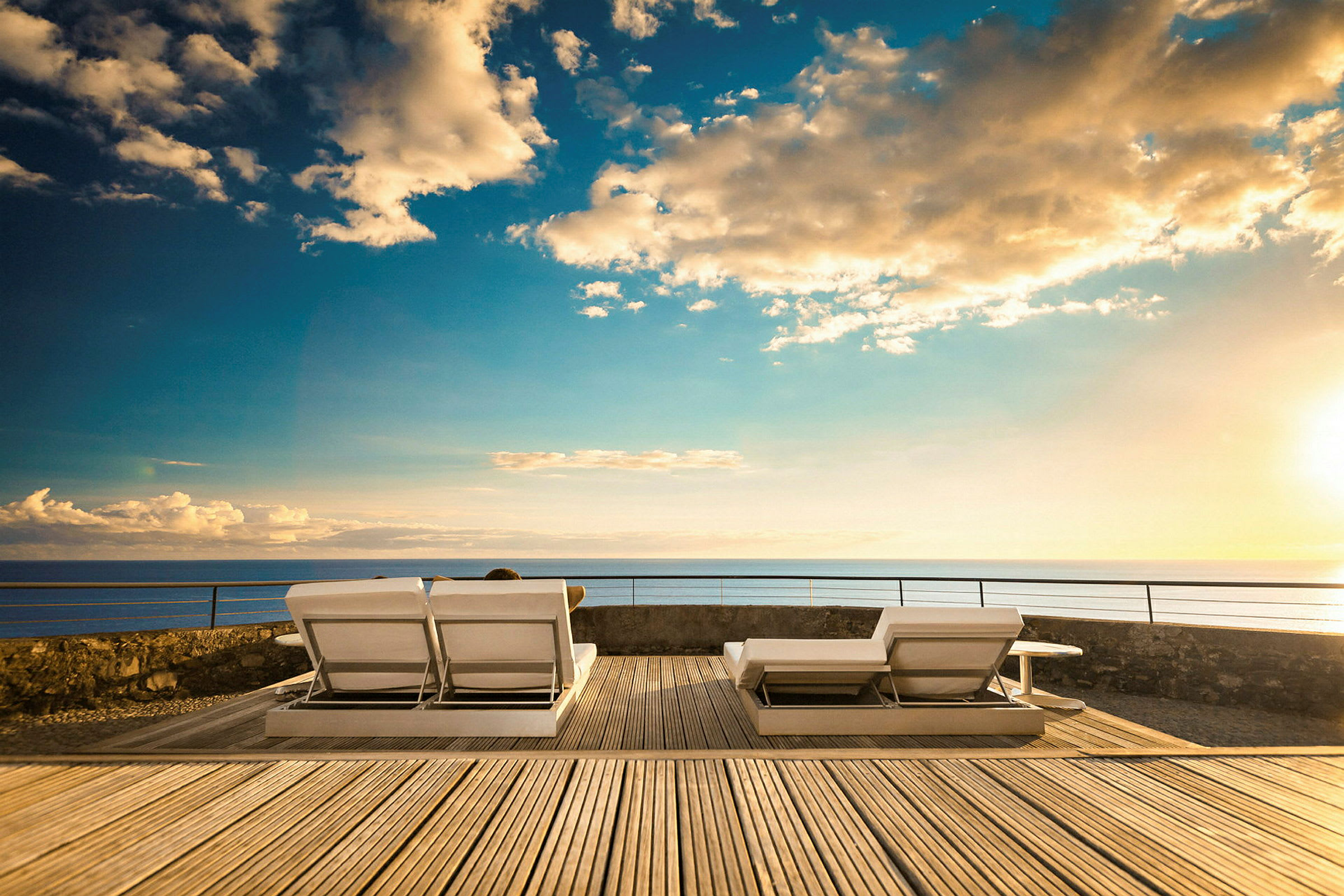 To solsenger på en treterrasse med havutsikt ved solnedgang. (AI-generert tekst)