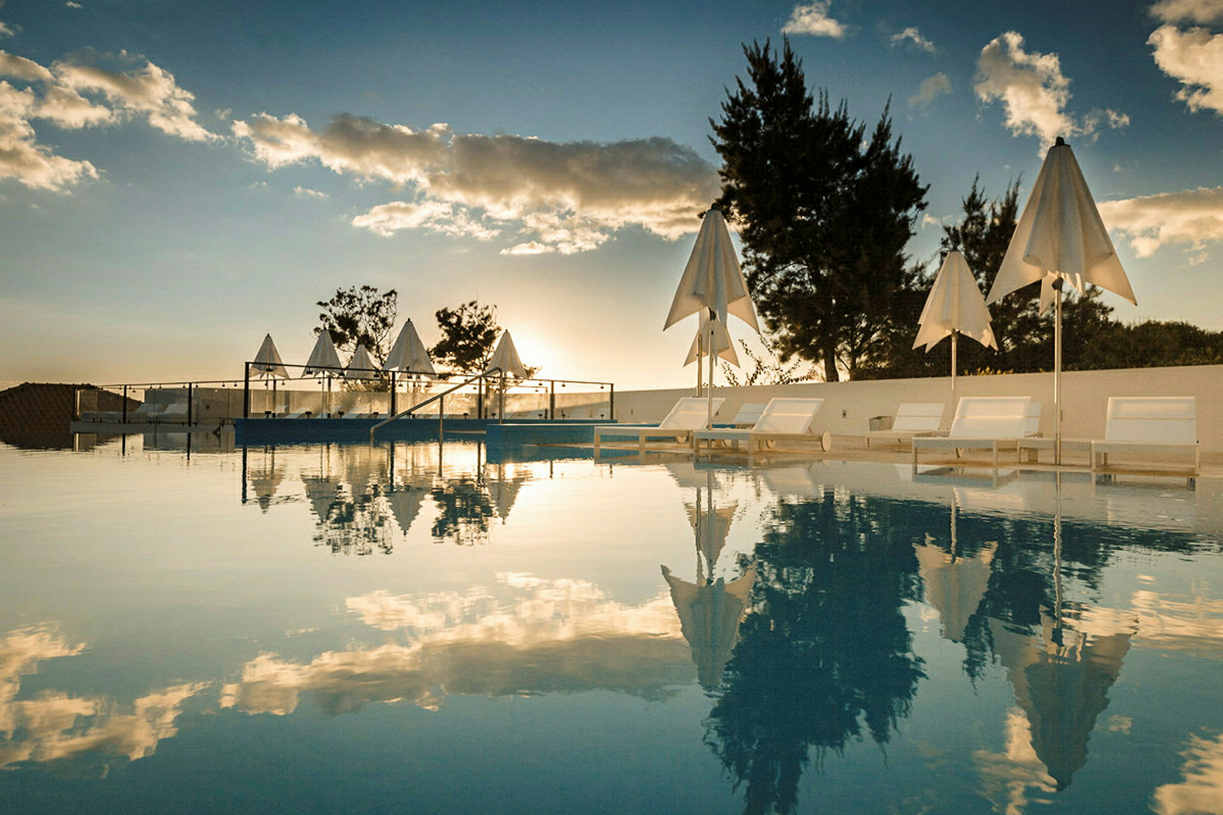 Bilde av et basseng med solsenger og parasoller ved solnedgang. (AI-generert tekst)