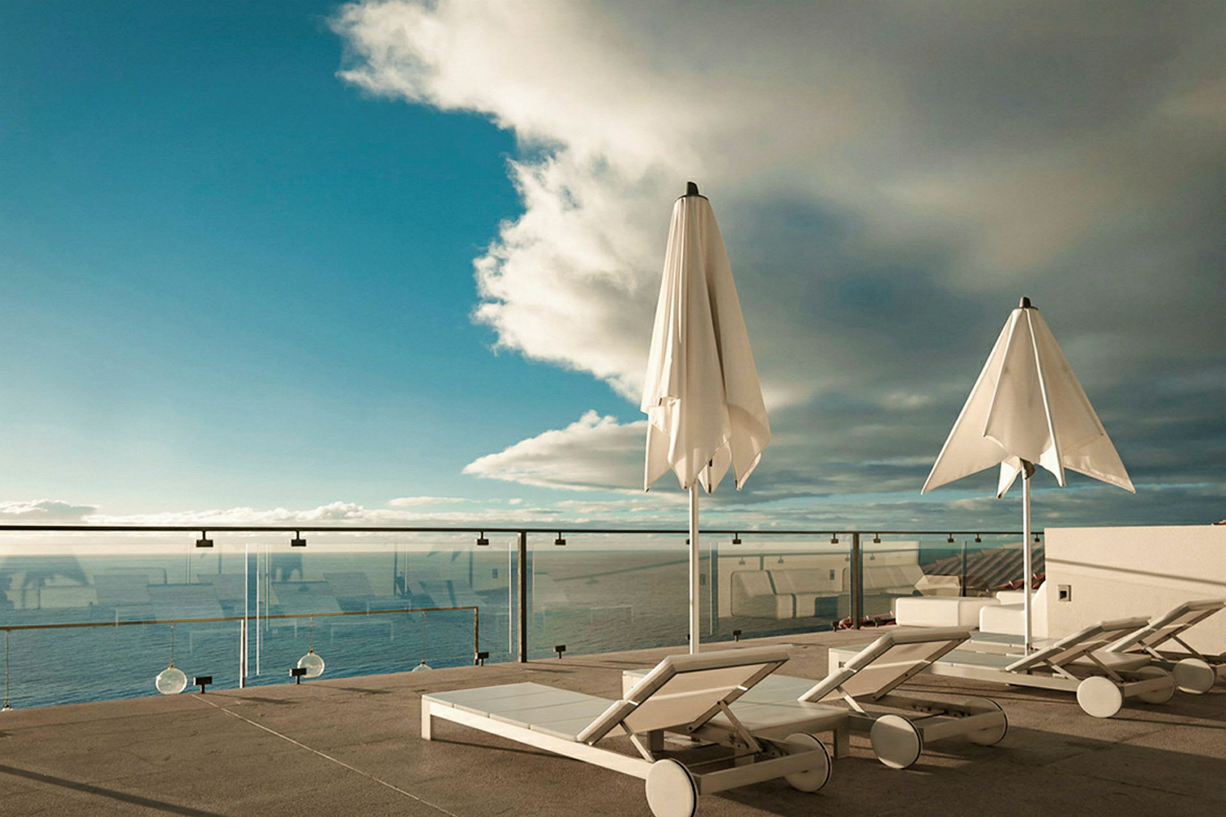 Bilde av en terrasse med solsenger, parasoller og utsikt over havet. (AI-generert tekst)