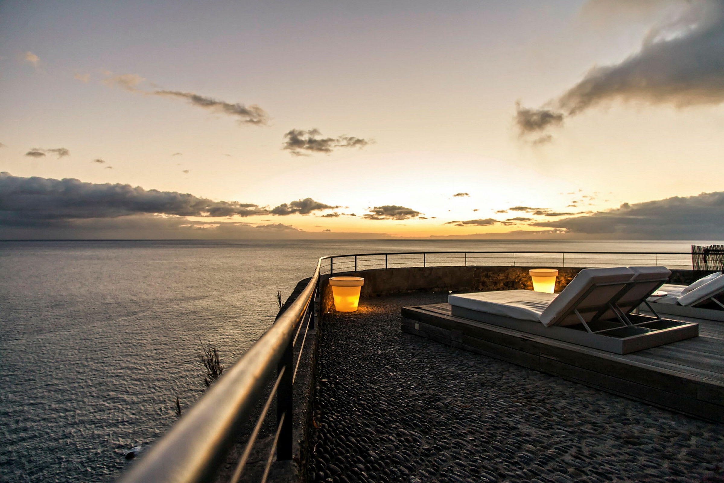 Terrasse ved havet med solsenger og en lampe i solnedgang. (AI-generert tekst)