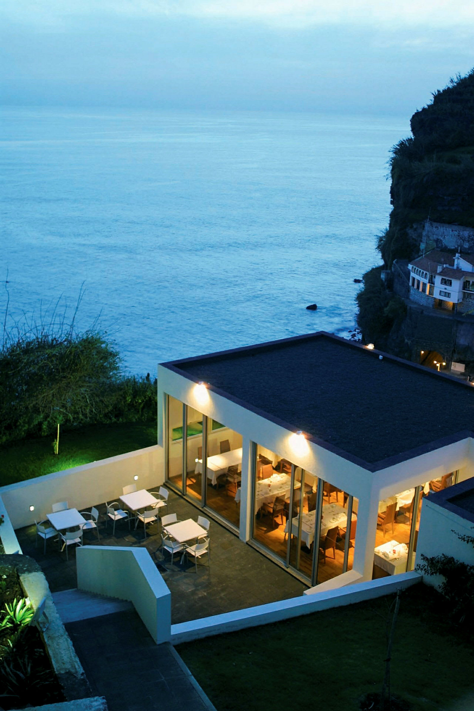 Moderne restaurant ved havet med terrasse for utendørs servering. (AI-generert tekst)