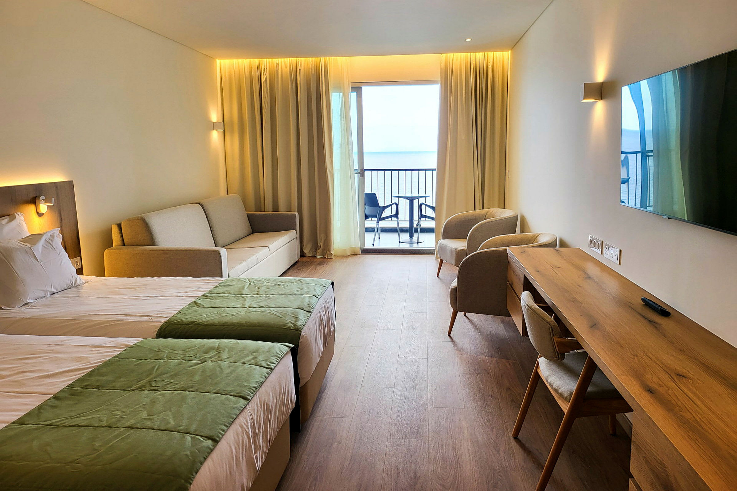Et hotellrom med to senger, sofa, to lenestoler, skrivebord og en balkong med utsikt. (AI-generert tekst)