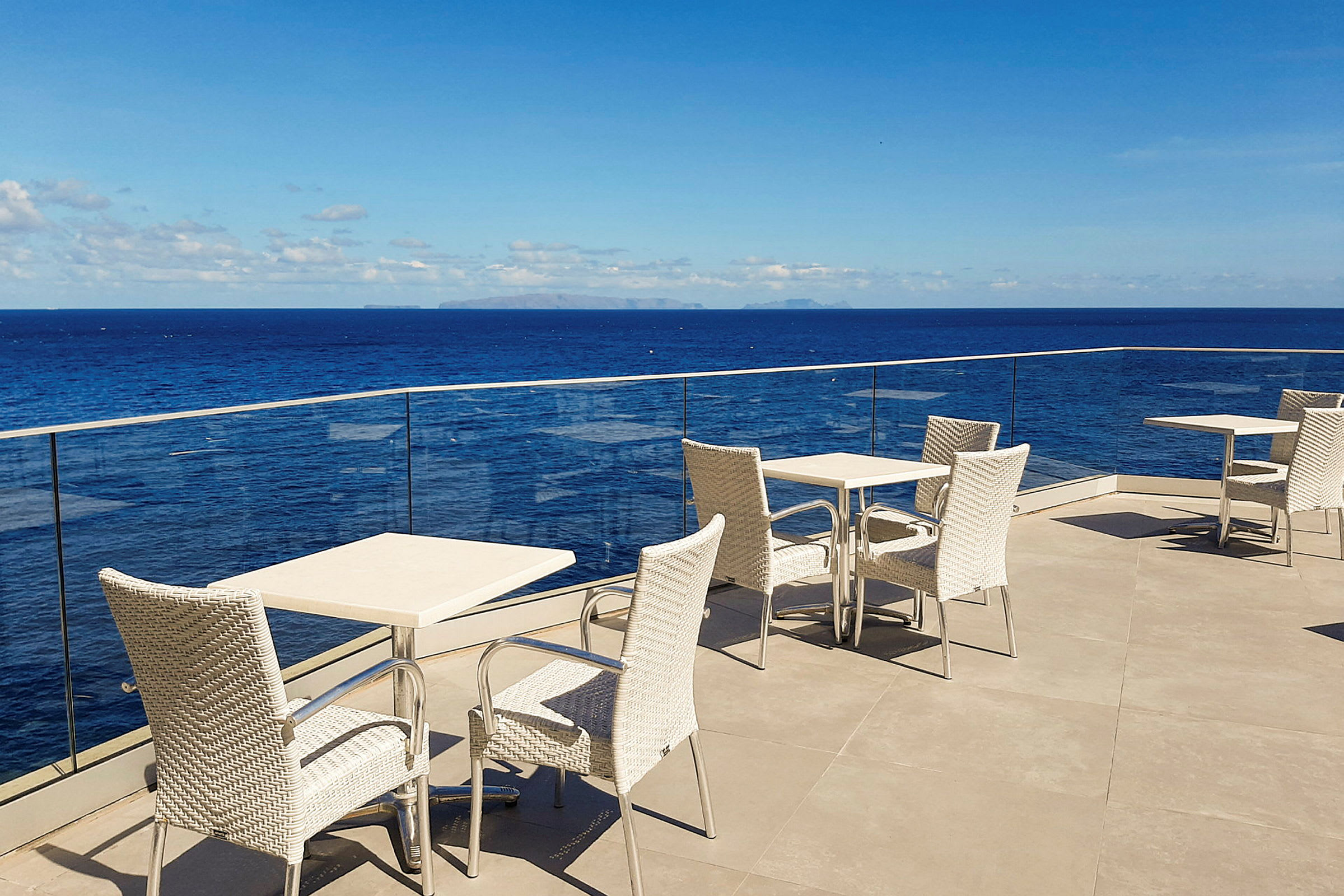 Bord- og stoler på en terrasse med utsikt over havet og blå himmel. (AI-generert tekst)