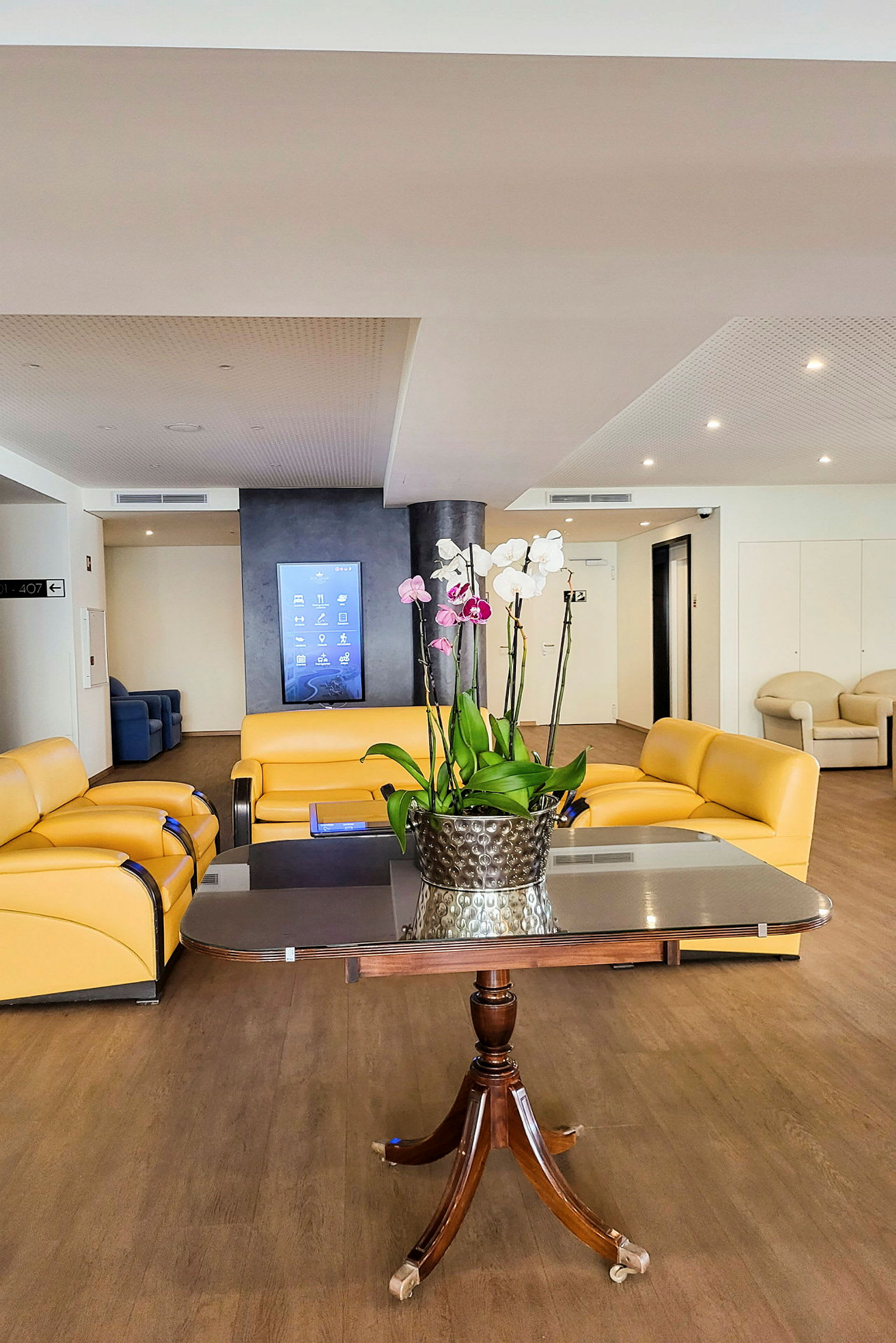 En hotellobby med gule sofaer, et bord og en blomsterpotte med orkideer. (AI-generert tekst)