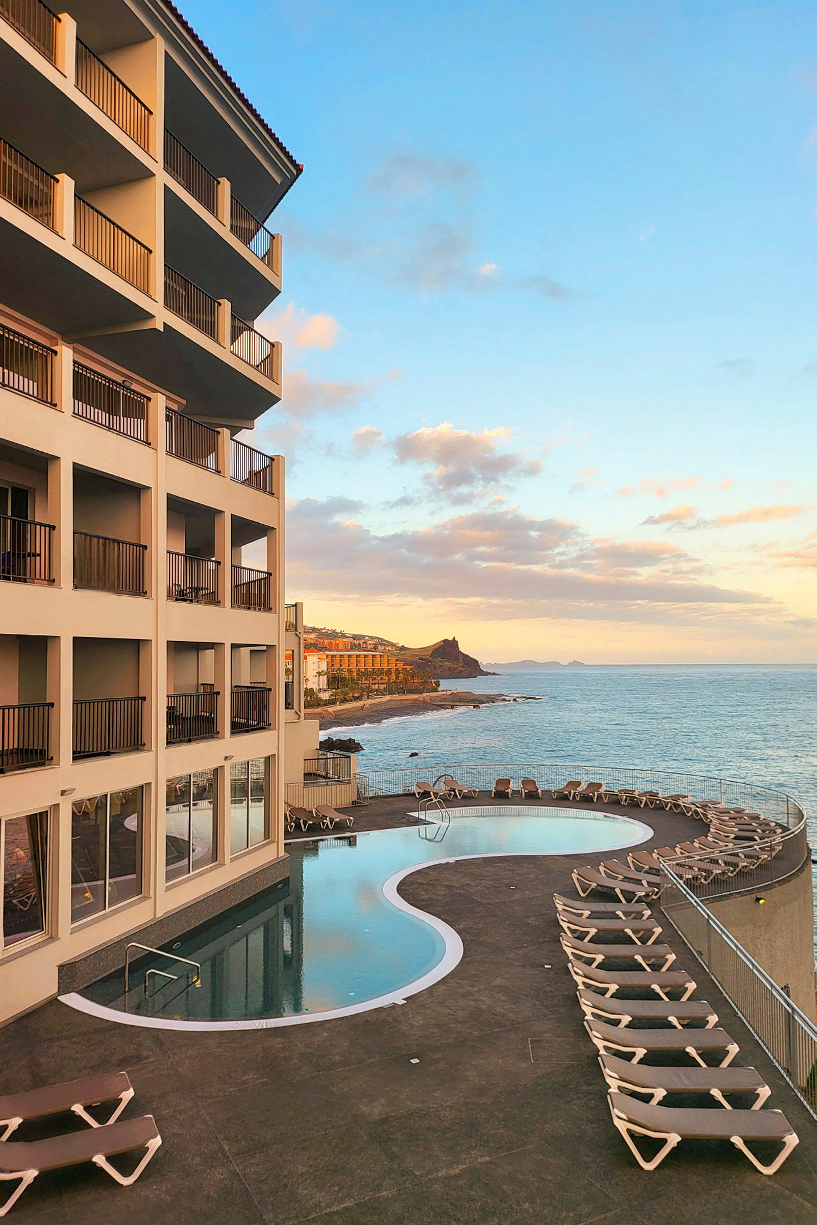 Et hotell med et svømmebasseng og solsenger ved havet under en klar himmel. (AI-generert tekst)