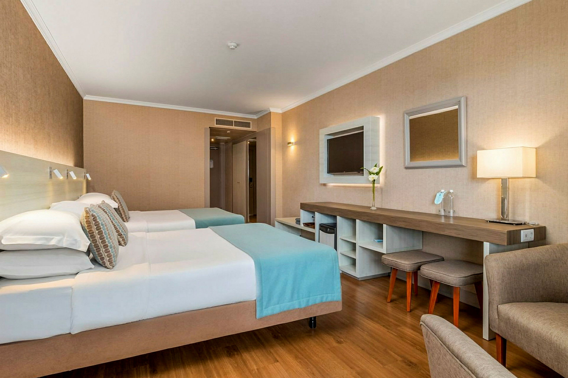 Hotellrom med to enkeltsenger, arbeidsområde og sittemøbler. (AI-generert tekst)