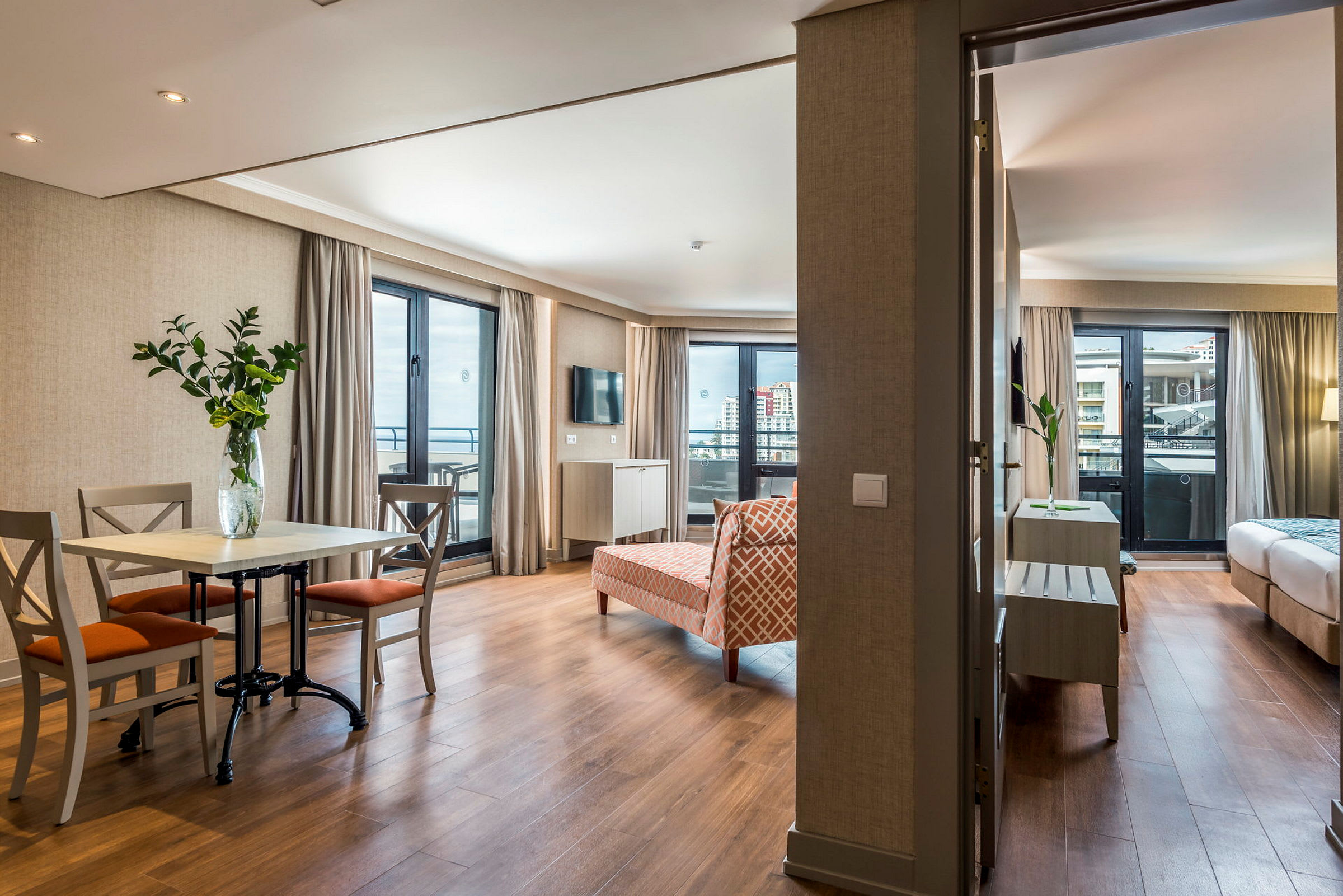 Et hotellrom med en stue inkludert spisebord og stoler, samt et soverom synlig i bakgrunnen. (AI-generert tekst)