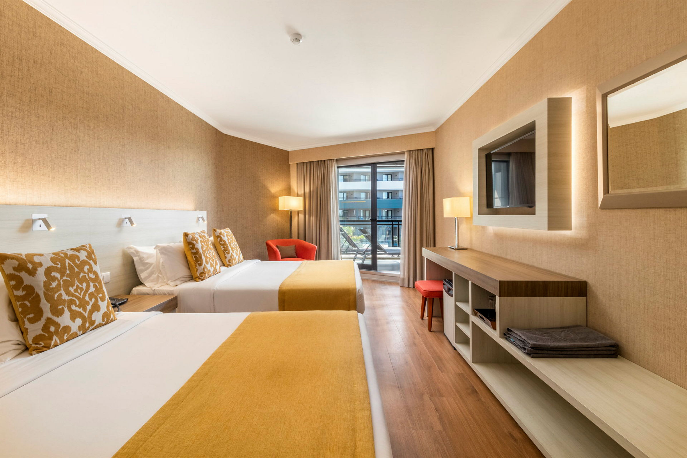Hotellrom med to senger, en lenestol og utsikt mot balkong. (AI-generert tekst)