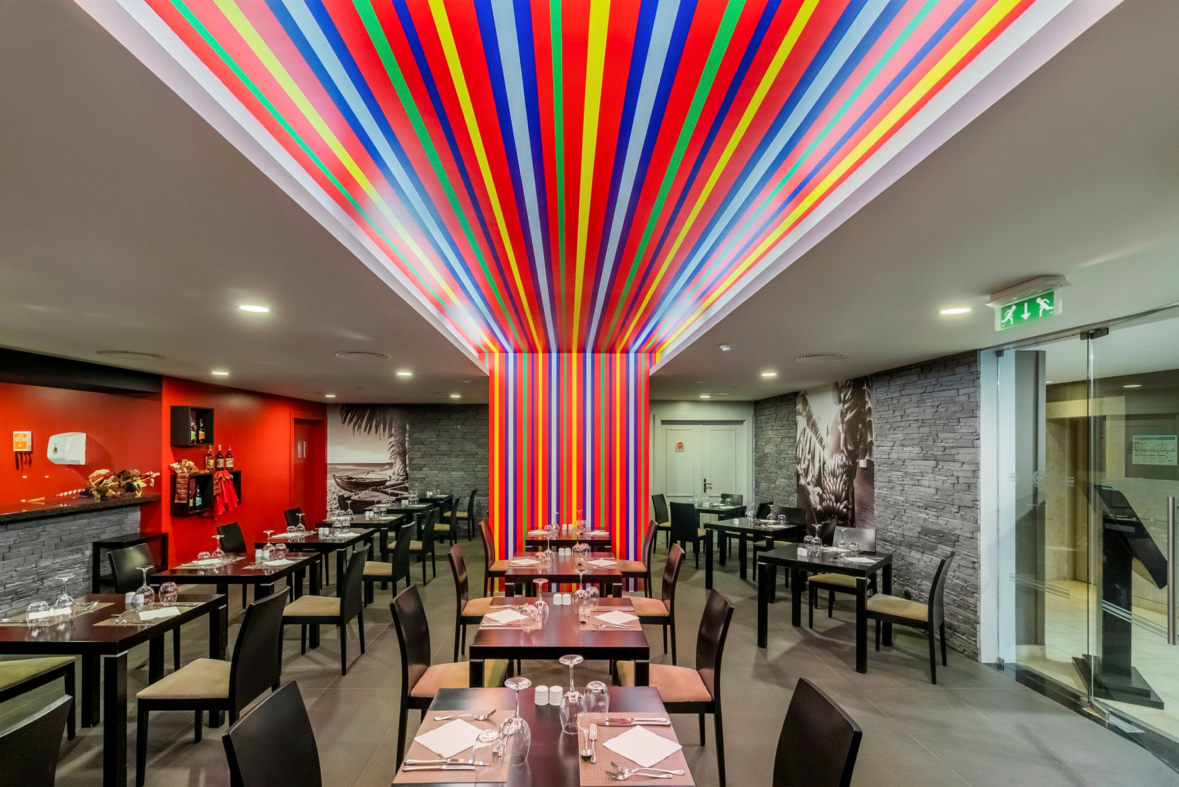En restaurant med bord og stoler og en fargerik dekor med striper på vegg og tak. (AI-generert tekst)