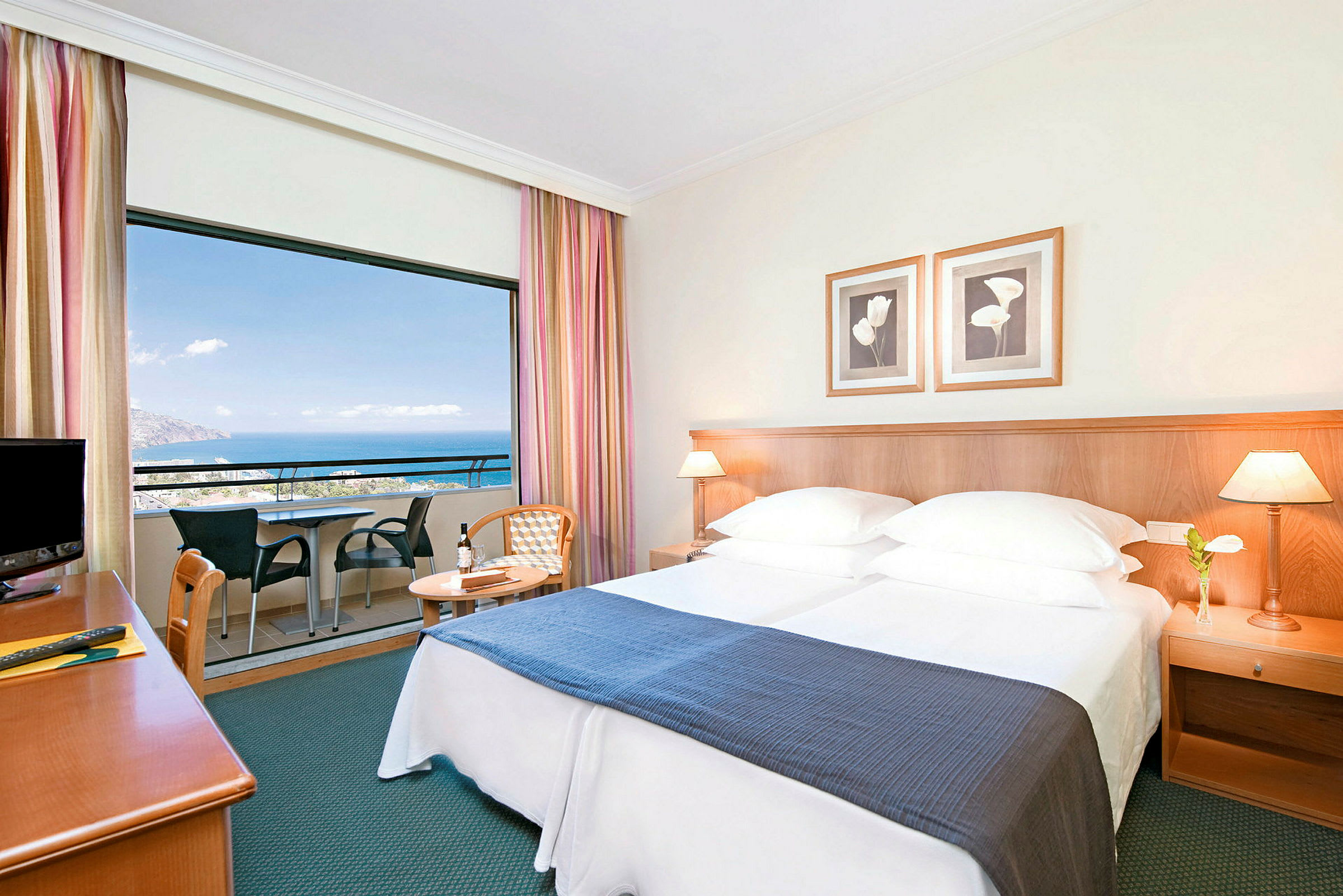 Hotellrom med dobbeltseng, nattbord og balkong med utsikt over havet. (AI-generert tekst)
