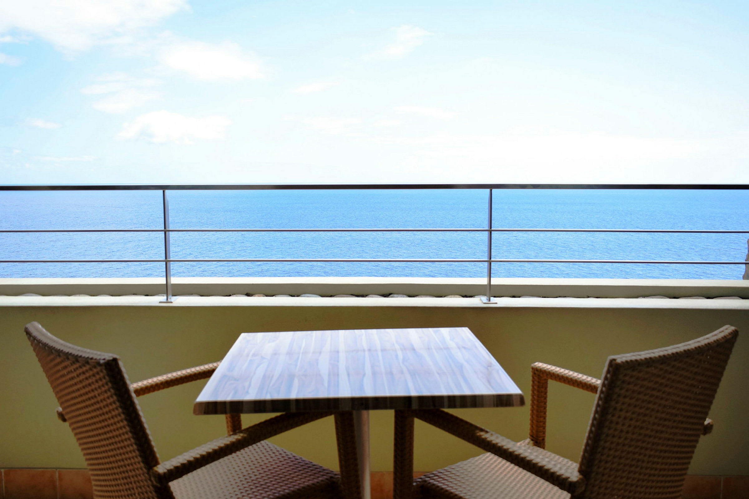 En utendørs terrasse med et bord og to stoler, med utsikt over havet. (AI-generert tekst)