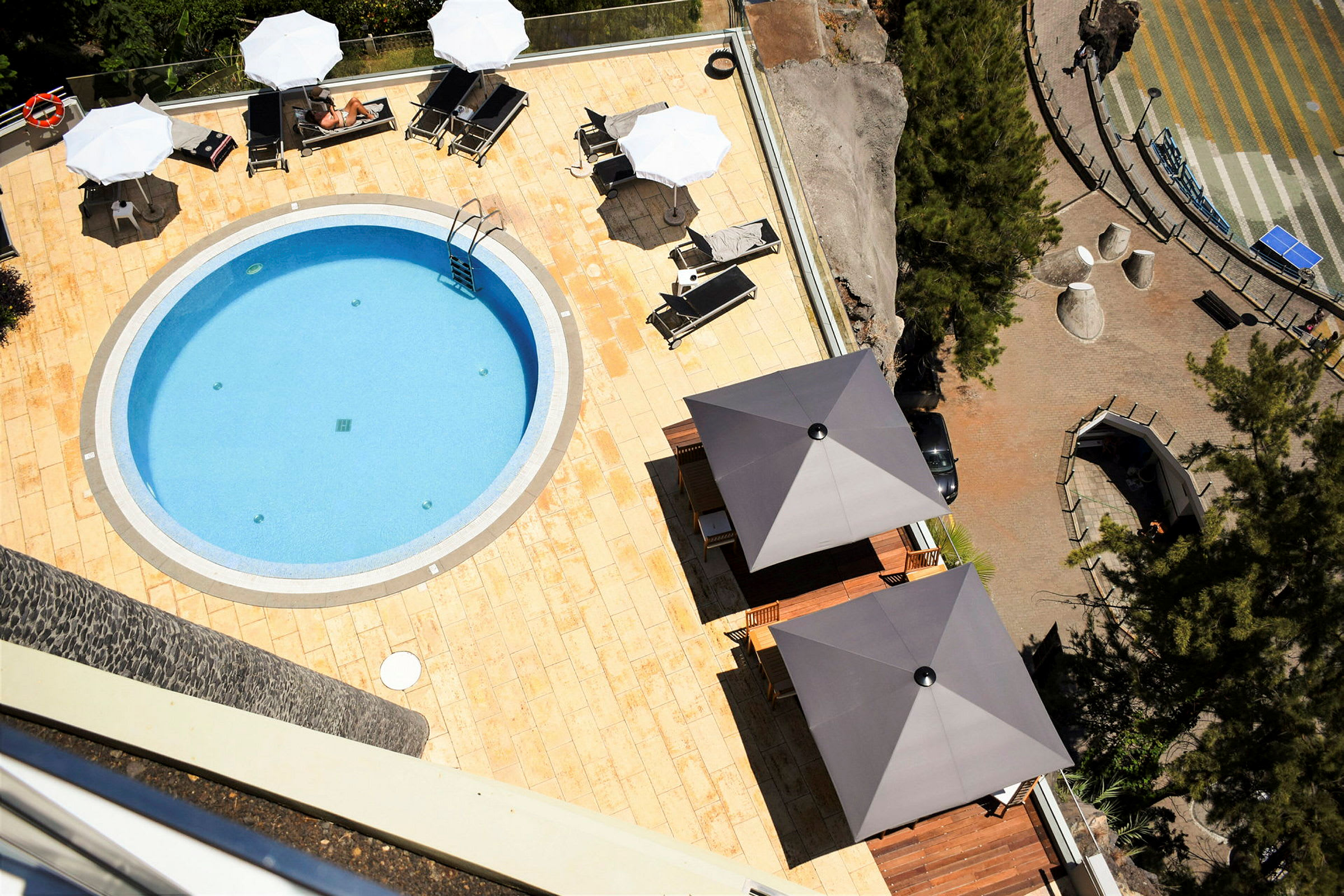 Et ovalt basseng omgitt av hvite steinplater på en solterrasse med parasoller og solsenger. (AI-generert tekst)