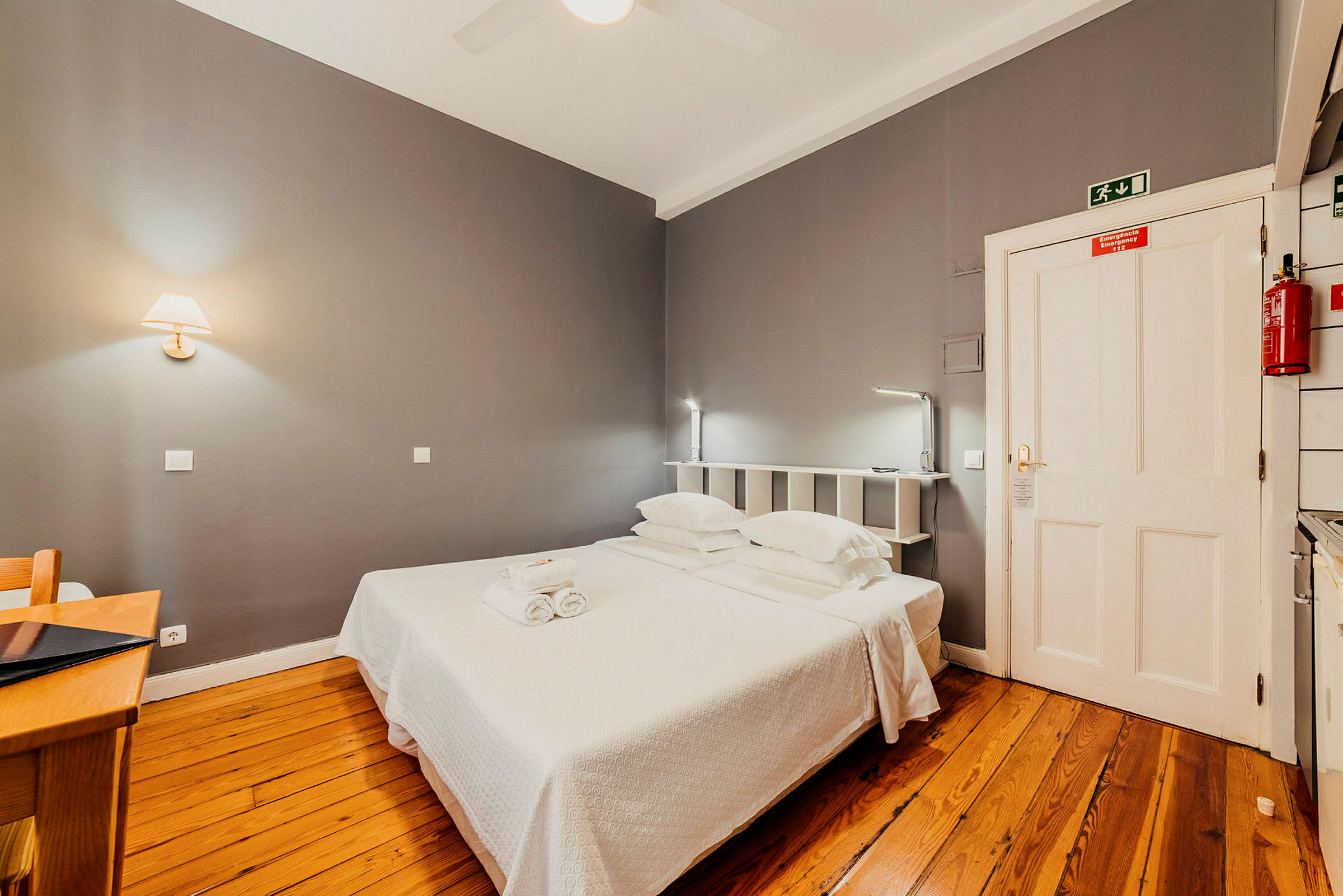 Hotellrom med grå vegger, tregulv og en dobbeltseng. (AI-generert tekst)