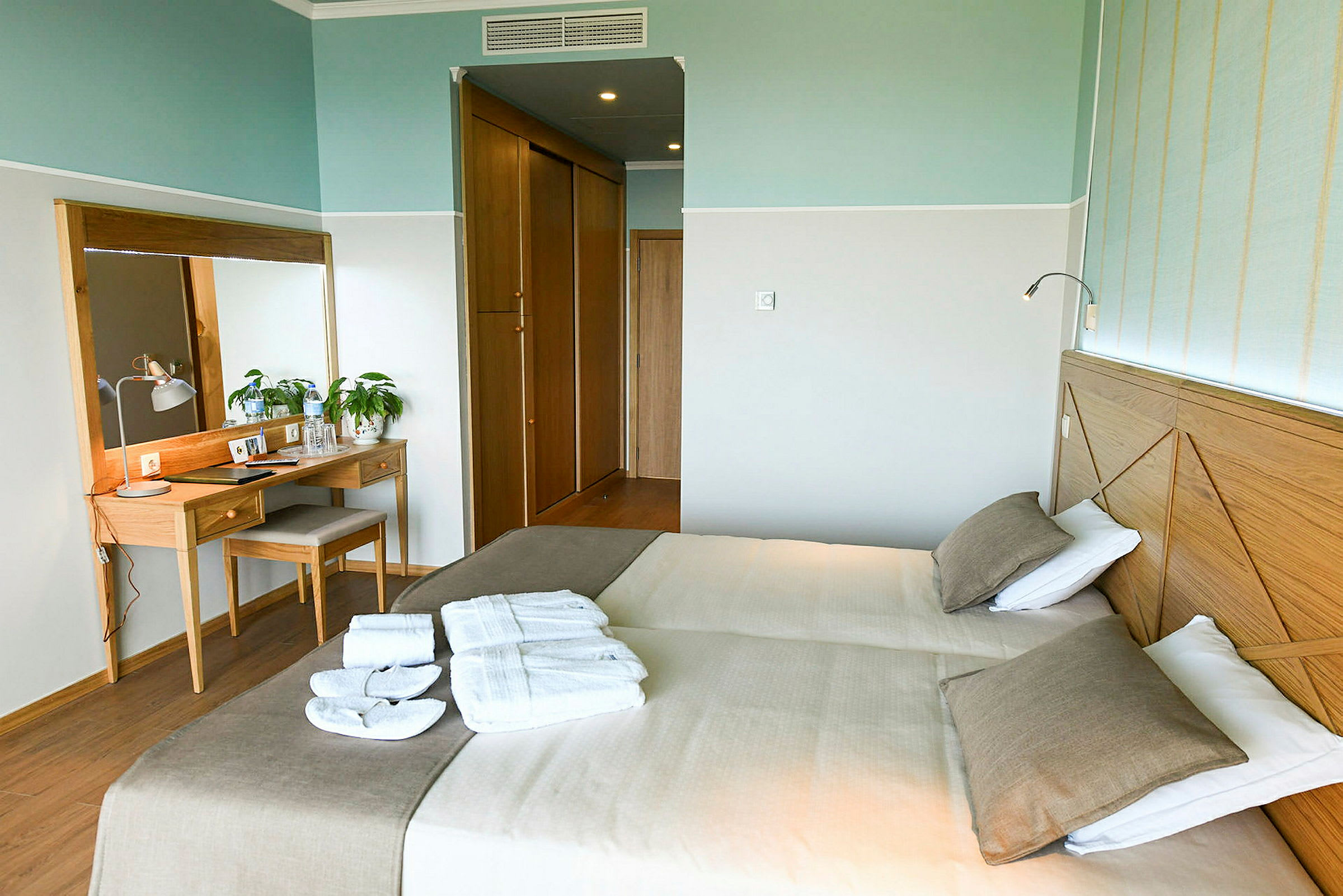 Hotellrom med to enkeltsenger, et speil og et skrivebord. (AI-generert tekst)