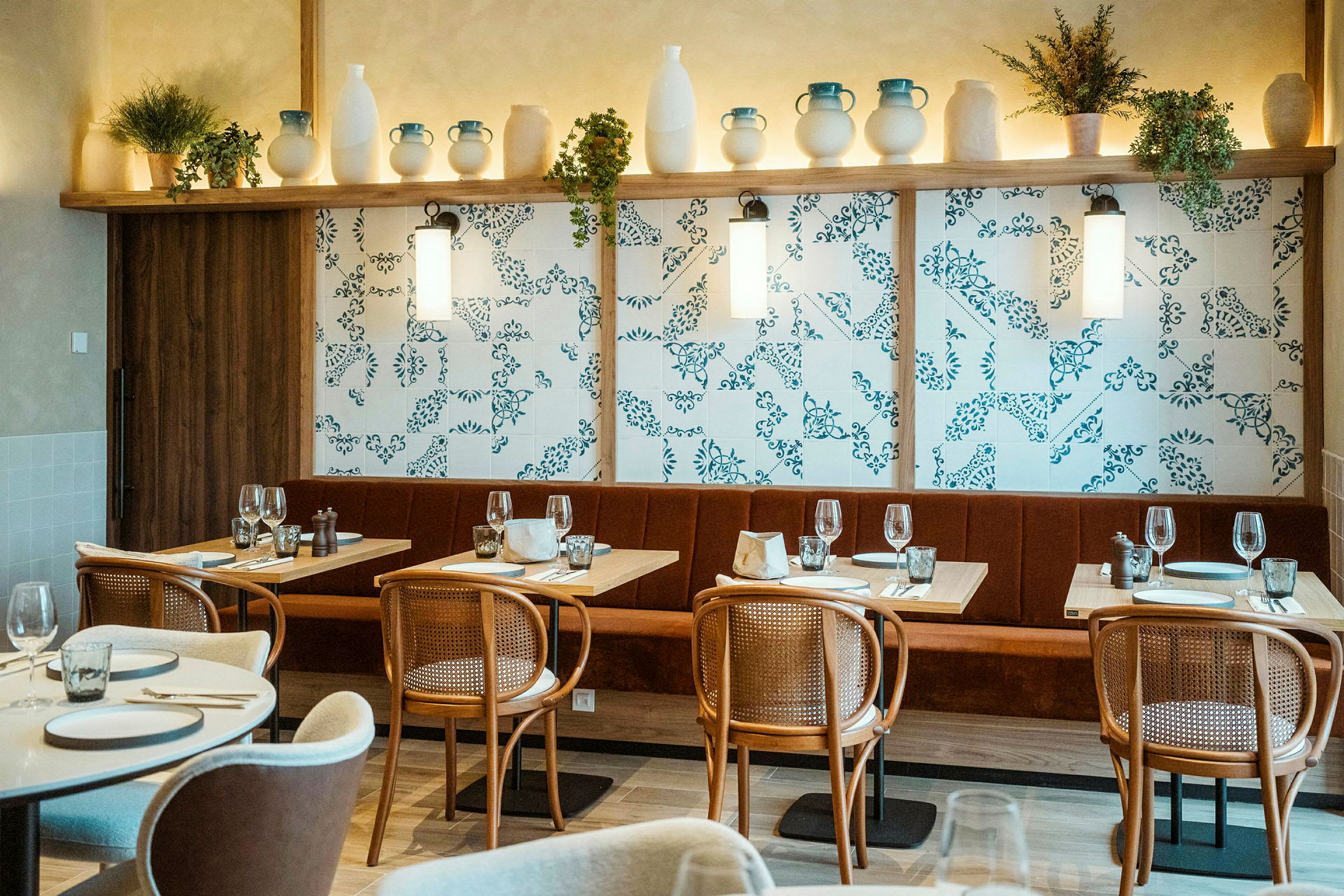 Et interiørbilde av en restaurant med dekkede bord, stoler og en dekorert vegg med hyller fylt med keramikk og planter. (AI-generert tekst)