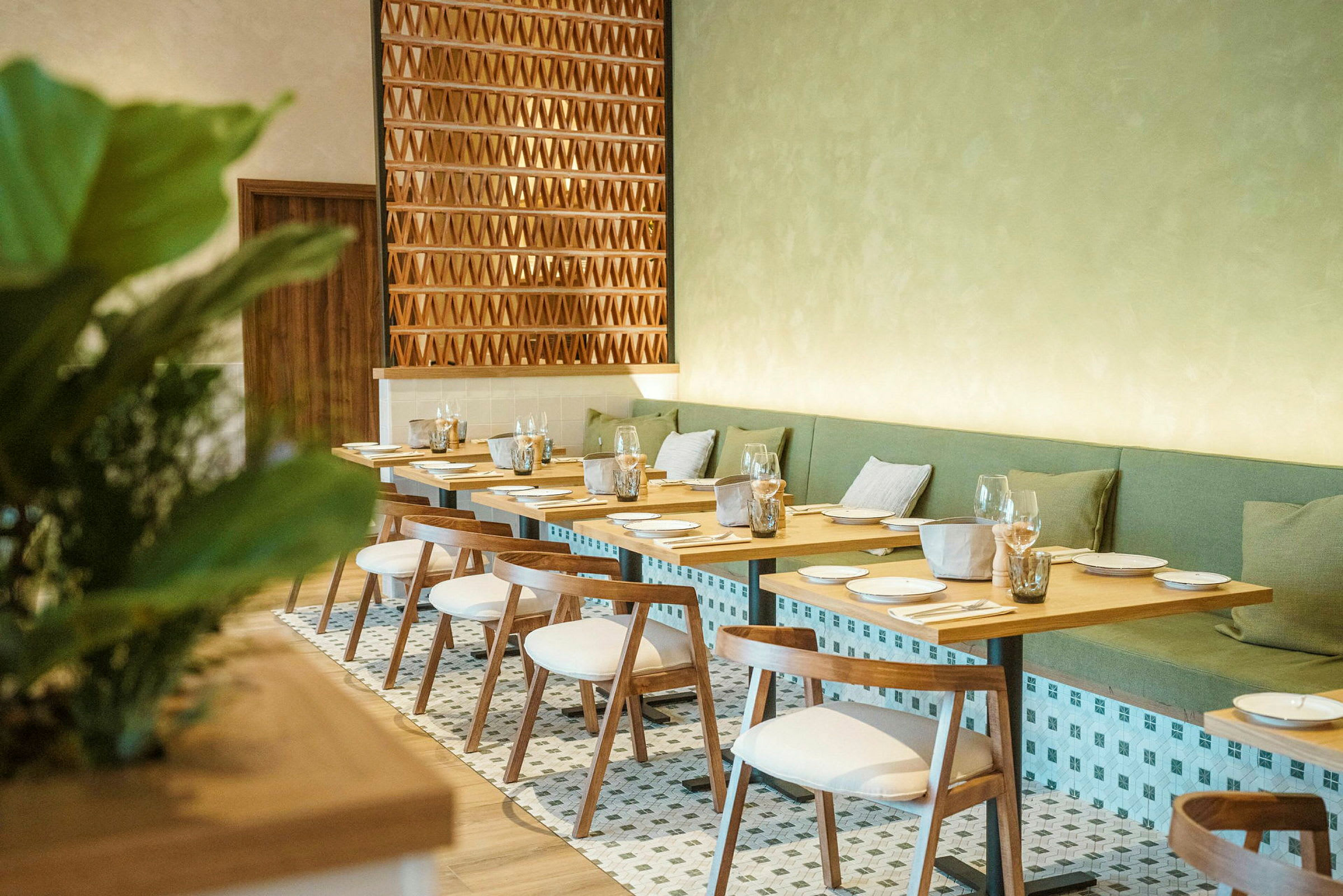 En elegant restaurant med trebord og hvite stoler samt grønne sitteputer mot veggen. (AI-generert tekst)