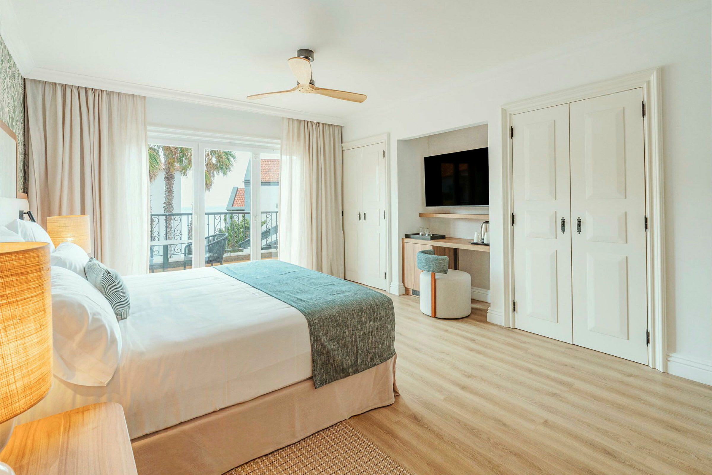 Et lyst, moderne hotellrom med en dobbeltseng, stort vindu, balkong og et ryddig skrivebord med TV. (AI-generert tekst)