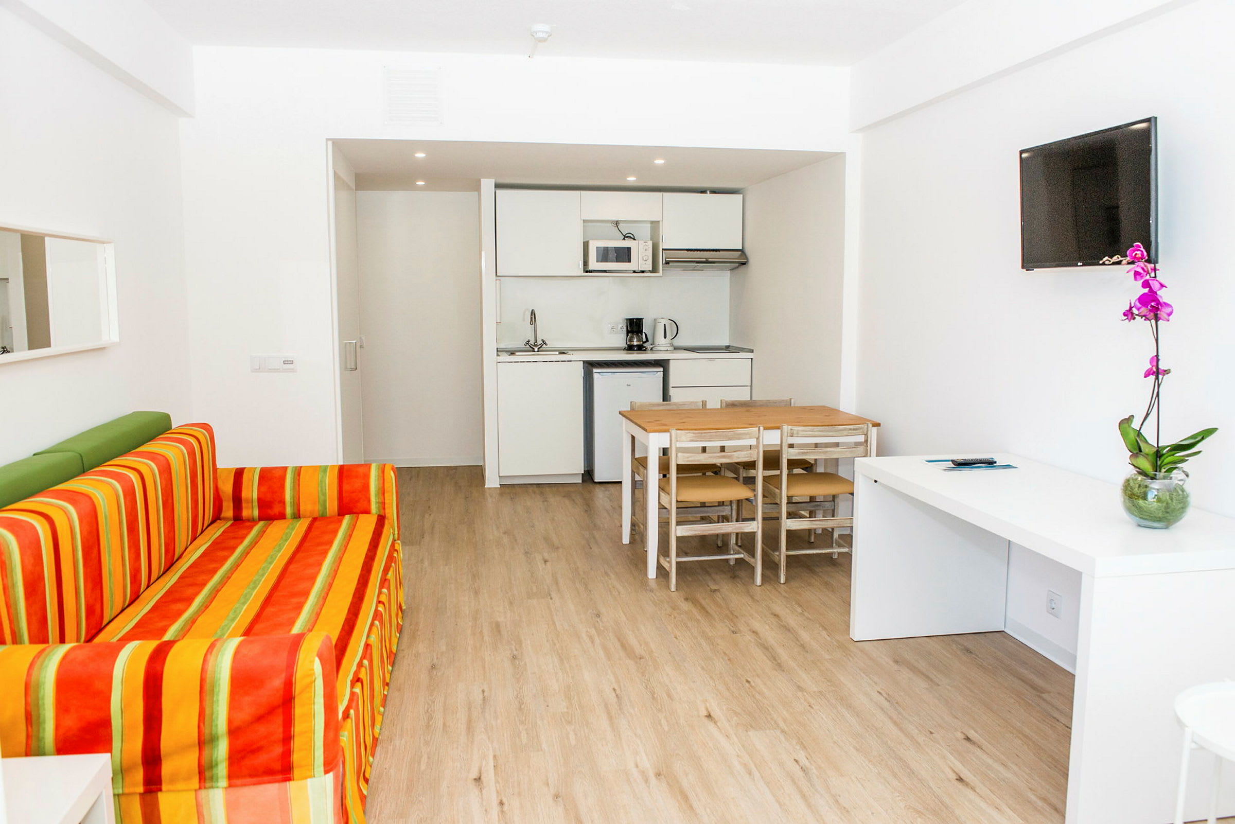 Bilde av et moderne hotellrom med sofa, spisebord, kjøkkenområde og TV. (AI-generert tekst)