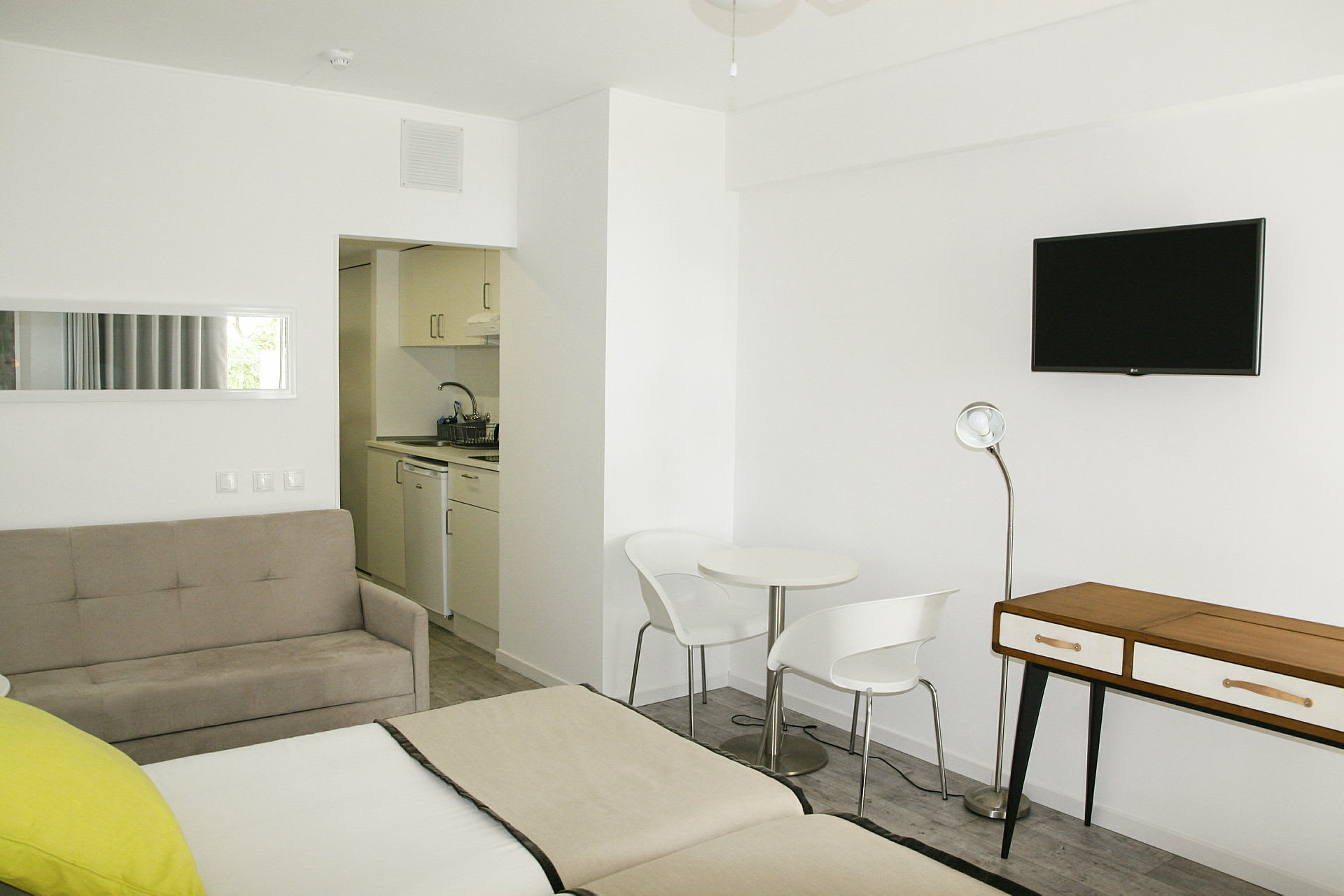 Et moderne hotellrom med hvite vegger, en sittegruppe og et mindre kjøkken. (AI-generert tekst)