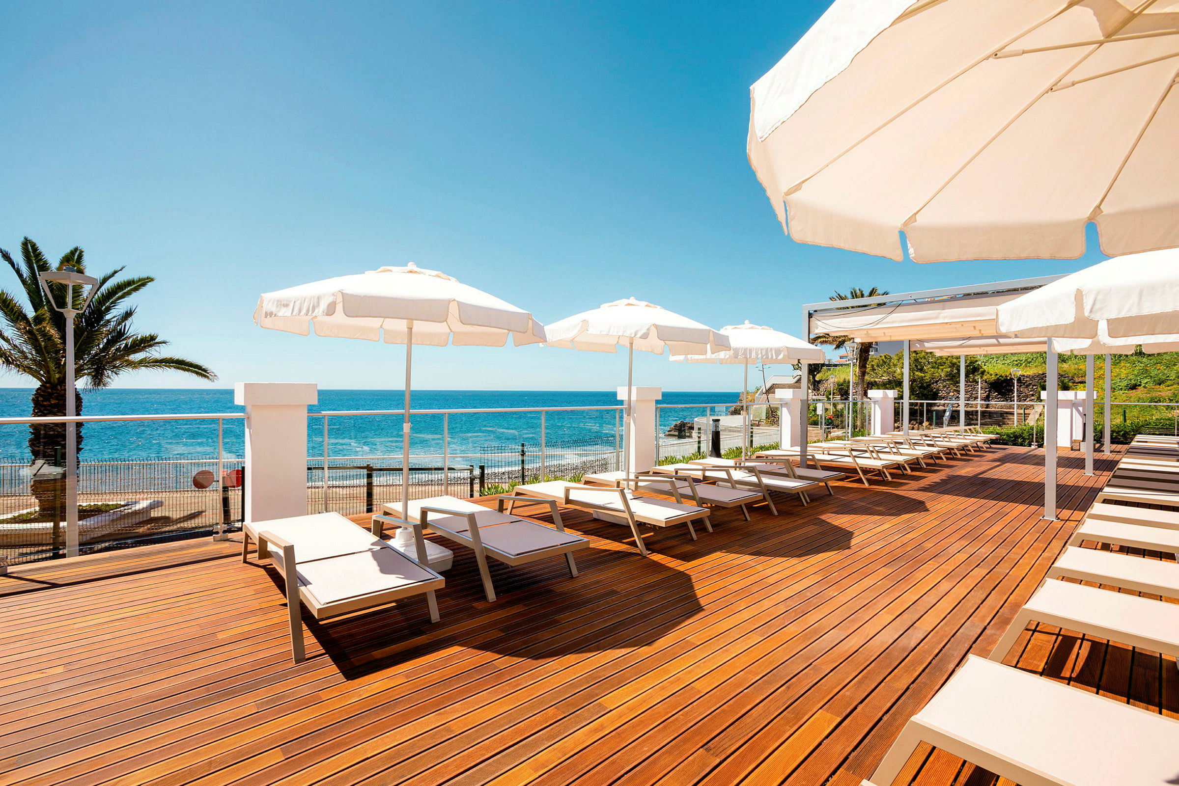 Solstoler og parasoller på en treterrasse ved havet. (AI-generert tekst)