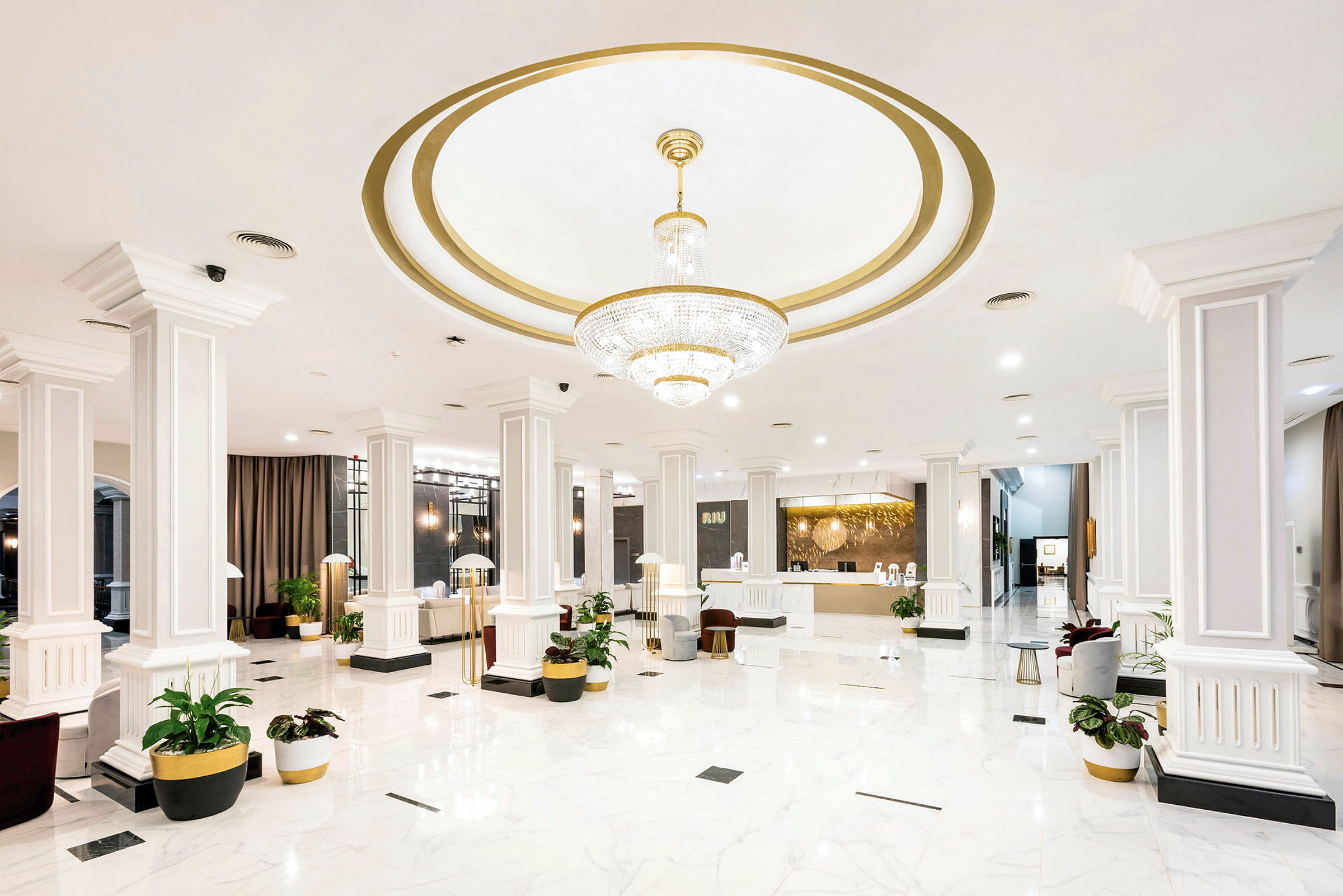 Hotellobbyen med hvit marmorgulv, søyler og en stor lysekrone. (AI-generert tekst)