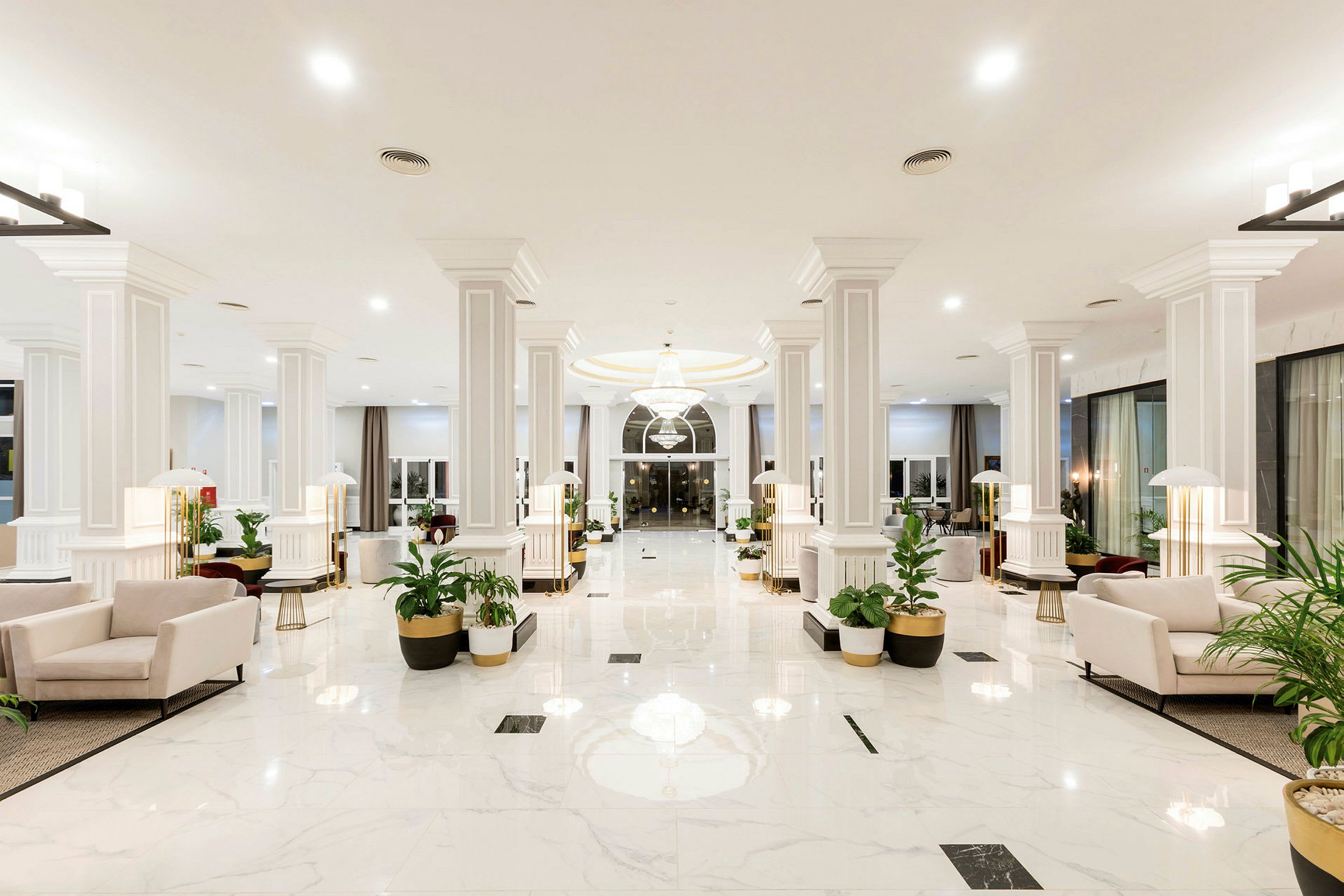 Lys og romslig hotellobby med hvite marmorgulv, lyse sittegrupper og grønne planter. (AI-generert tekst)