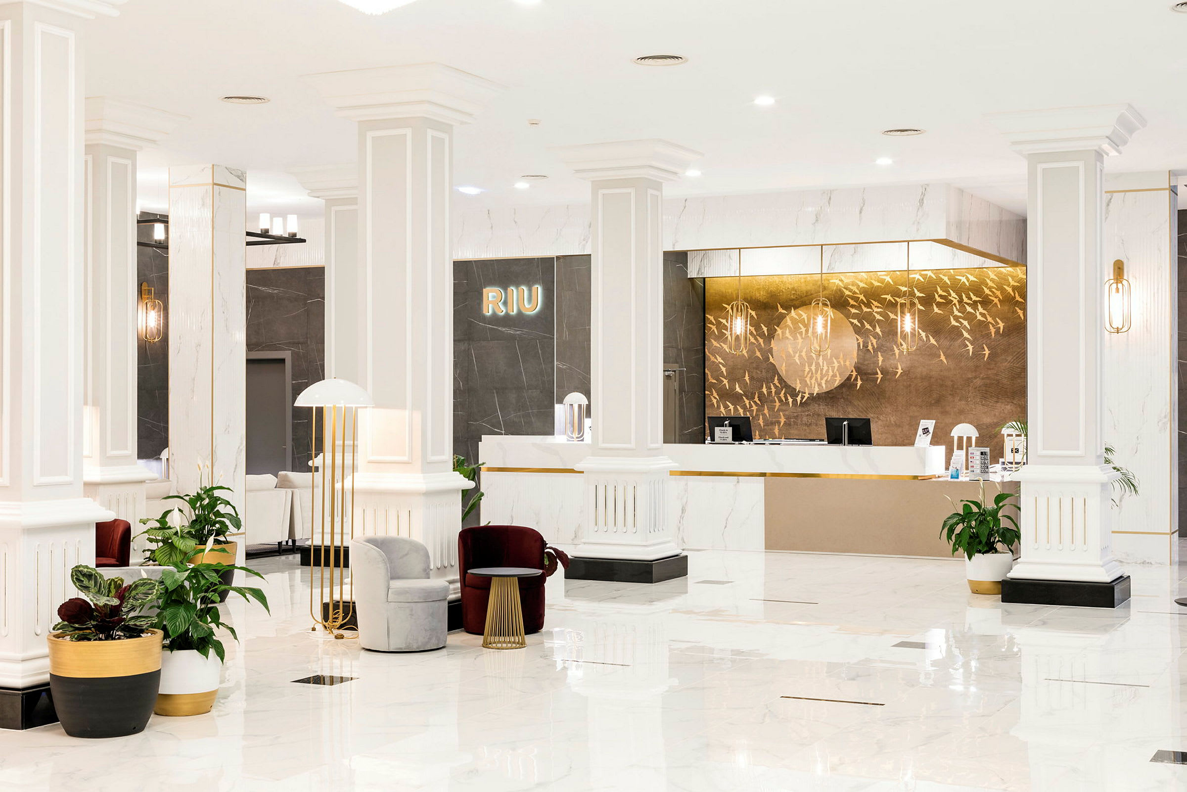 Resepsjonen i et Riu-hotell, moderne innredet med hvite søyler, gulv i lys marmor og elegante møbler. (AI-generert tekst)