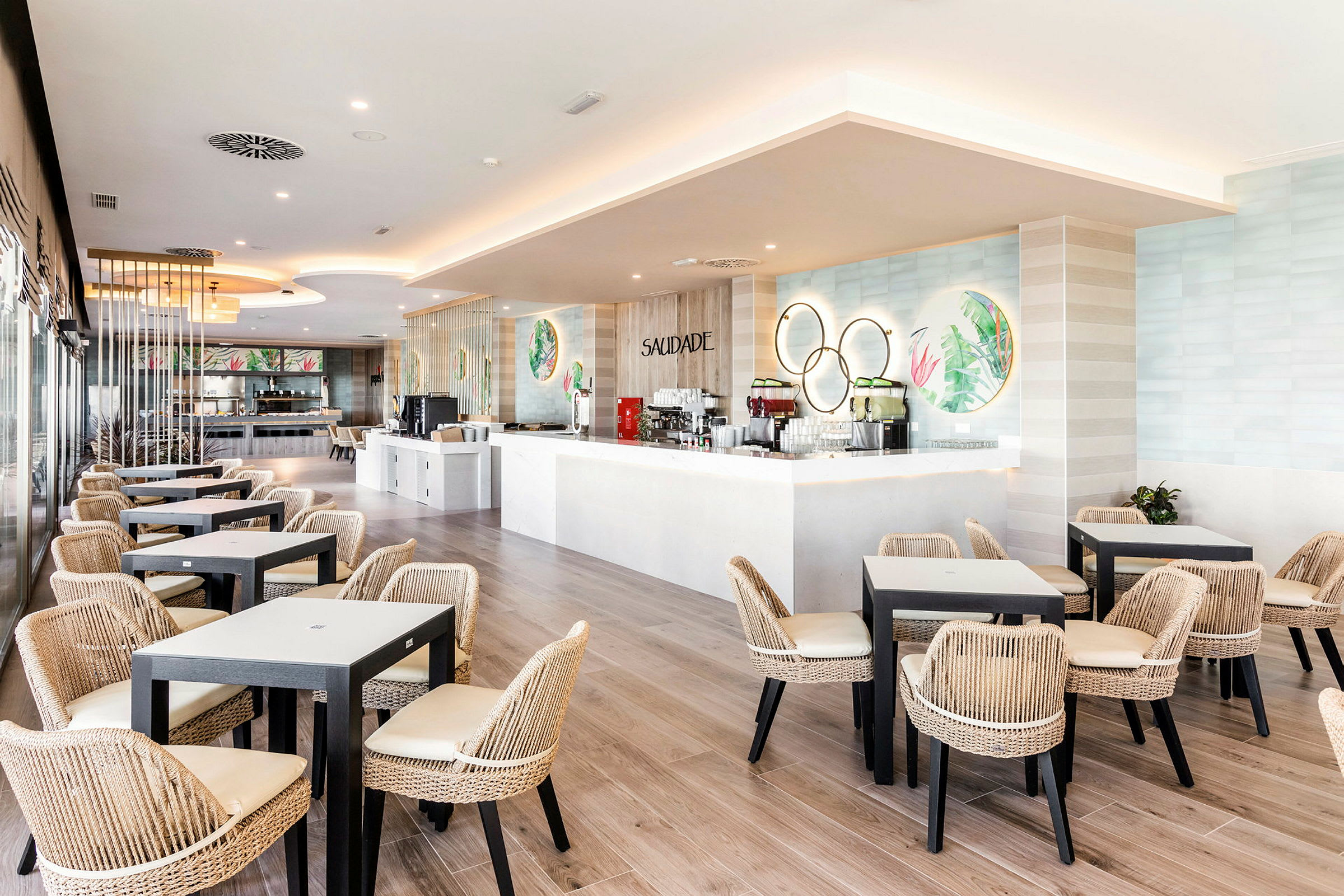 Lys restaurant med moderne bord og flettede stoler, samt en hvit bardisk. (AI-generert tekst)