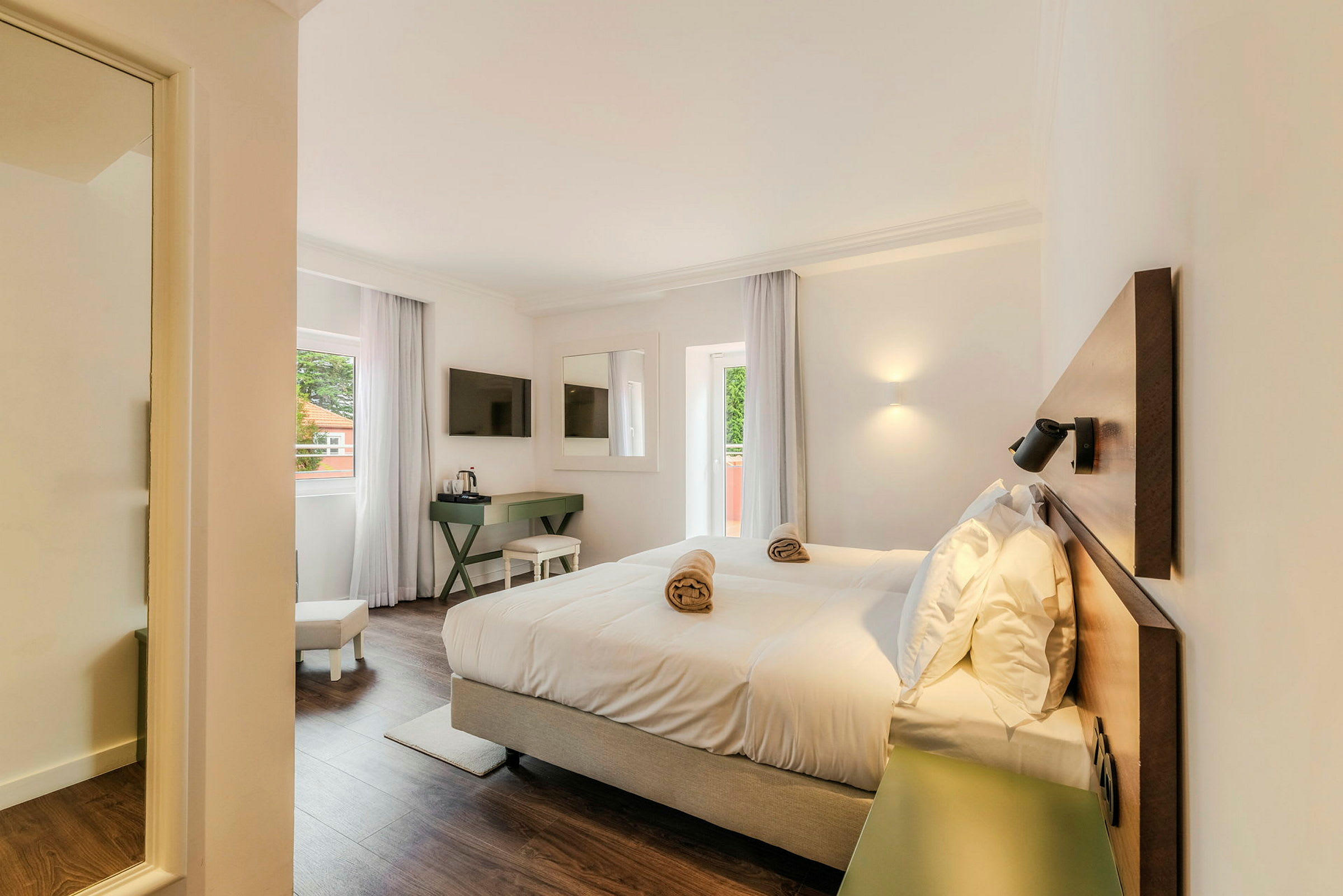 Et lyst hotellrom med en dobbeltseng, et vindu med gardiner, en TV på veggen og et skrivebord. (AI-generert tekst)