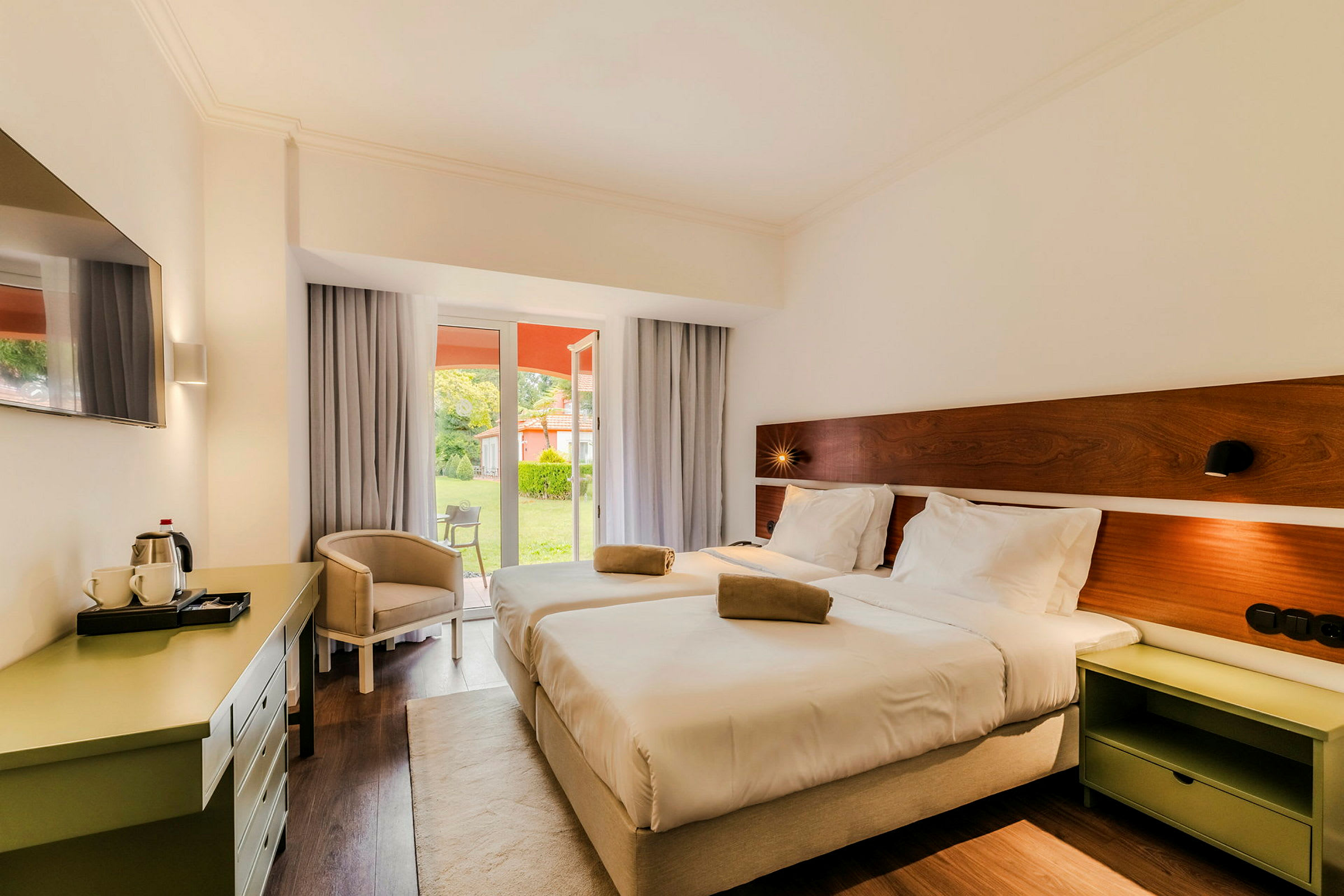Hotellrom med to senger som vender mot en vindusdør som fører til en frodig hage. (AI-generert tekst)