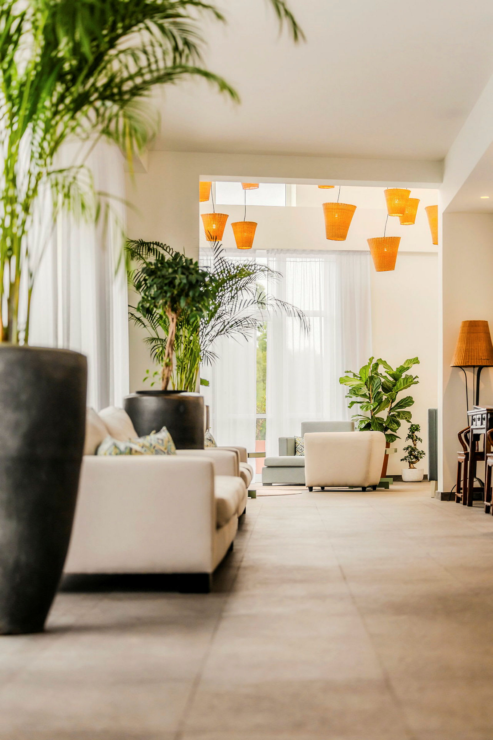 Et åpent rom med hvite sofaer, grønne potteplanter og oransje lamper som henger fra taket. (AI-generert tekst)