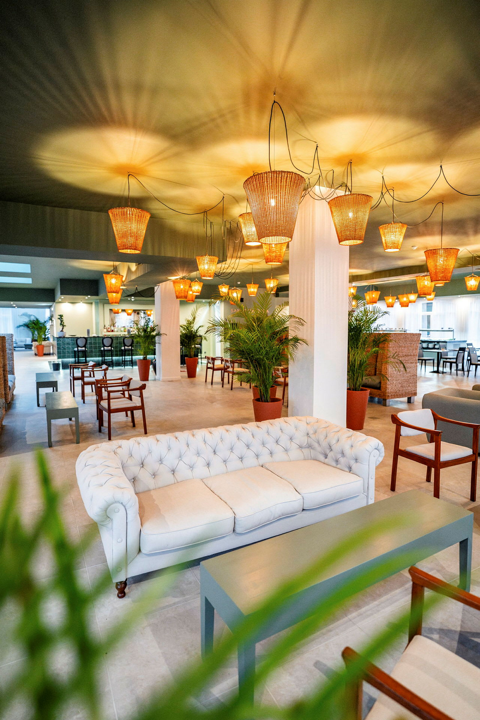 En stilfull lounge med en hvit sofa, tremøbler, grønne planter og taklamper av rotting. (AI-generert tekst)