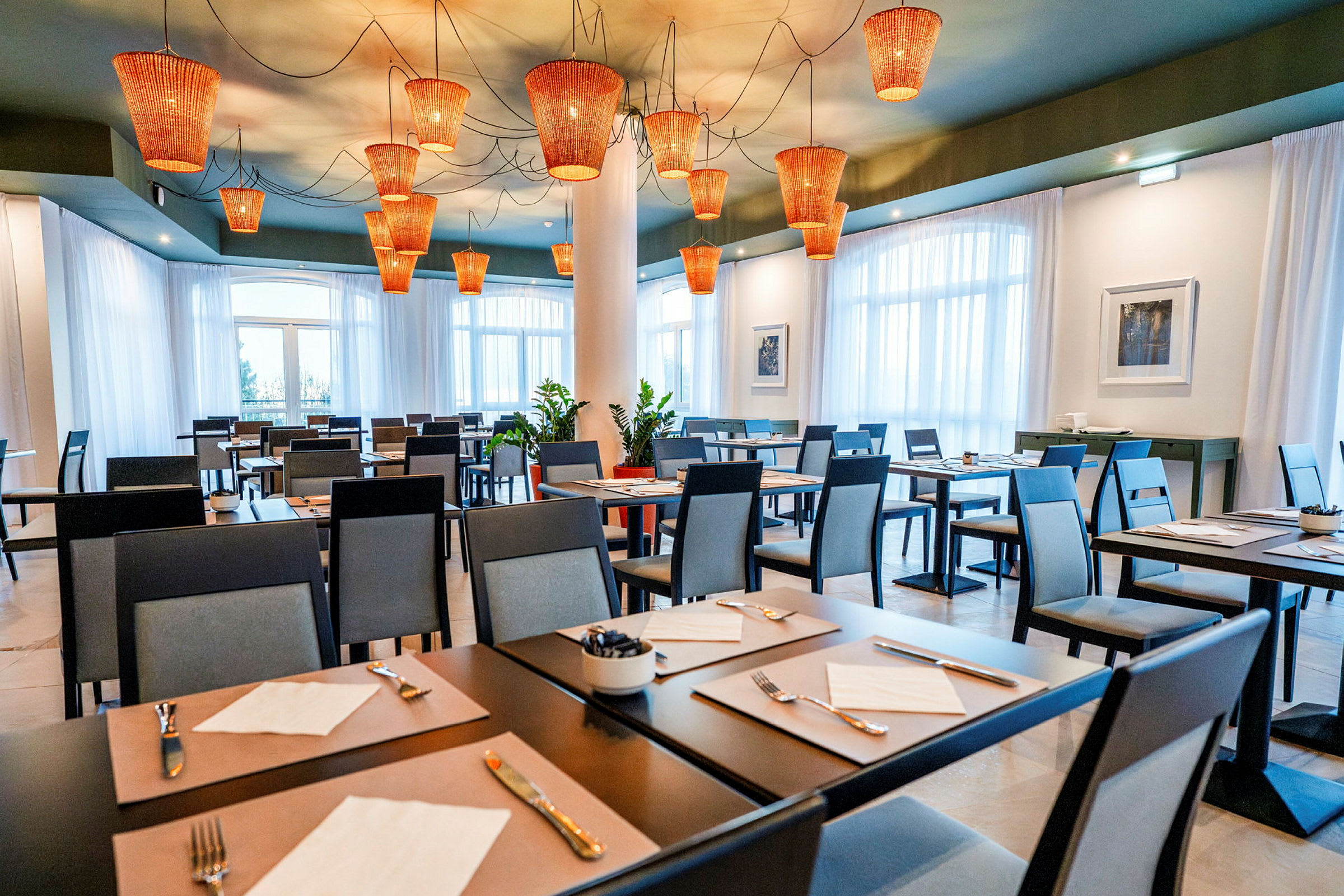 Restaurant med dekkede bord og moderne stoler, med oransje lamper i taket. (AI-generert tekst)