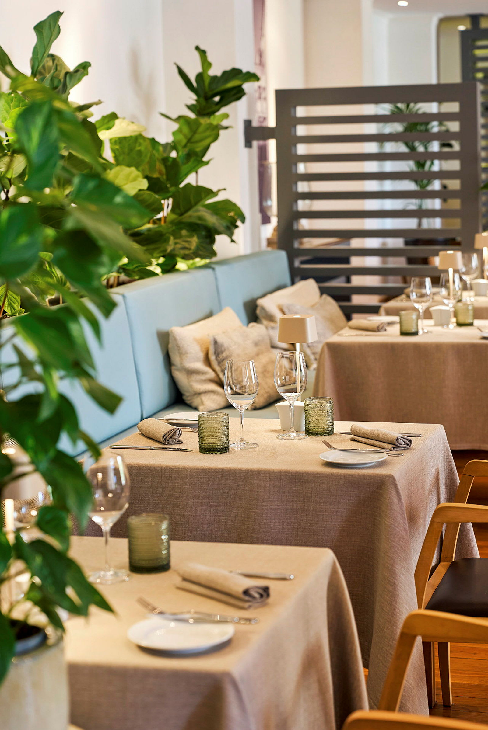 Et moderne restaurantbord med oppdekking i et lyst og innbydende miljø, omgitt av grønne planter. (AI-generert tekst)