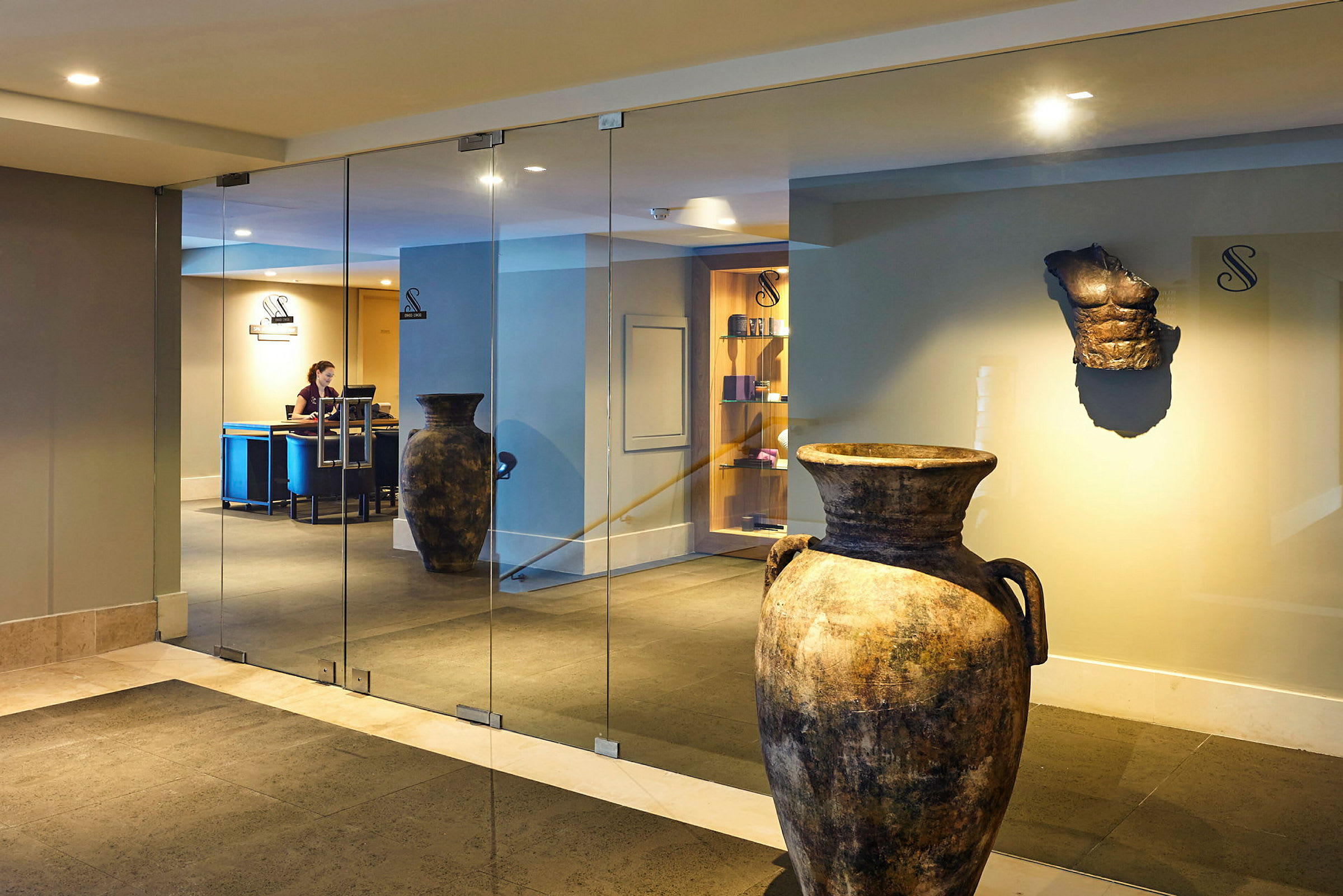 Keramikkrukker og en antikk skulptur i en hotellobby med glassvegger. (AI-generert tekst)
