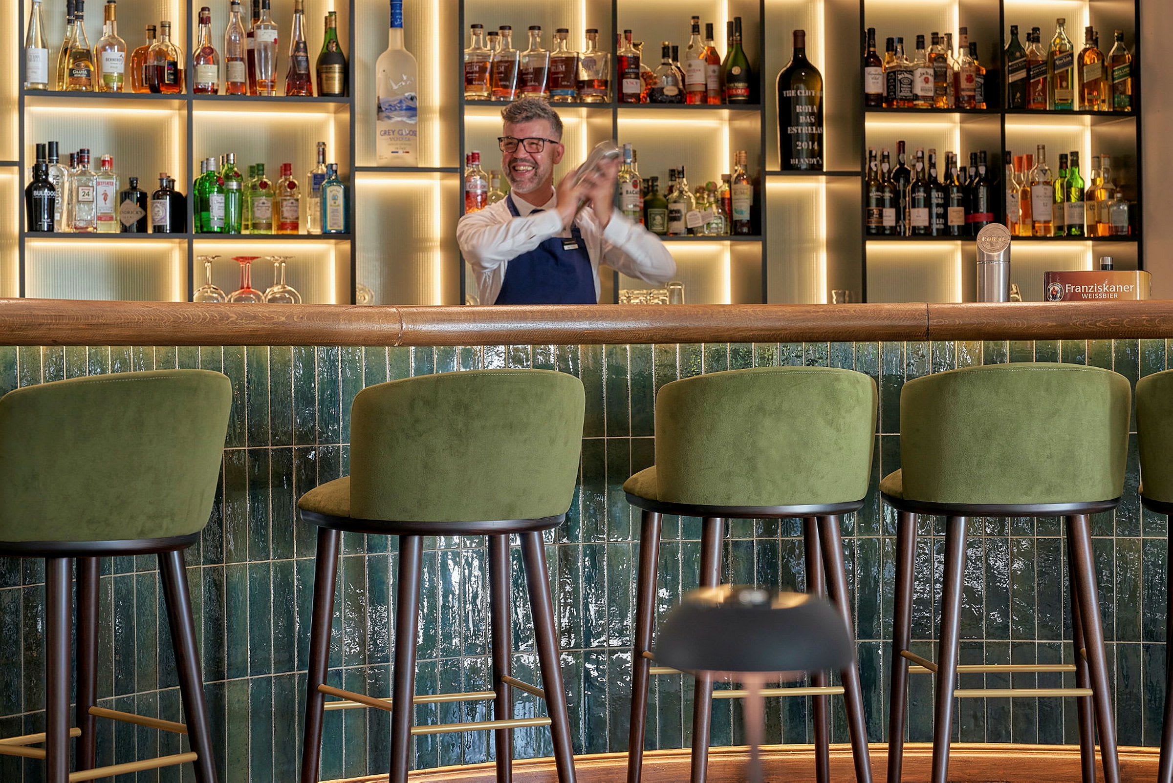 En bar med grønne barkrakker og en hylle med flasker i bakgrunnen. (AI-generert tekst)
