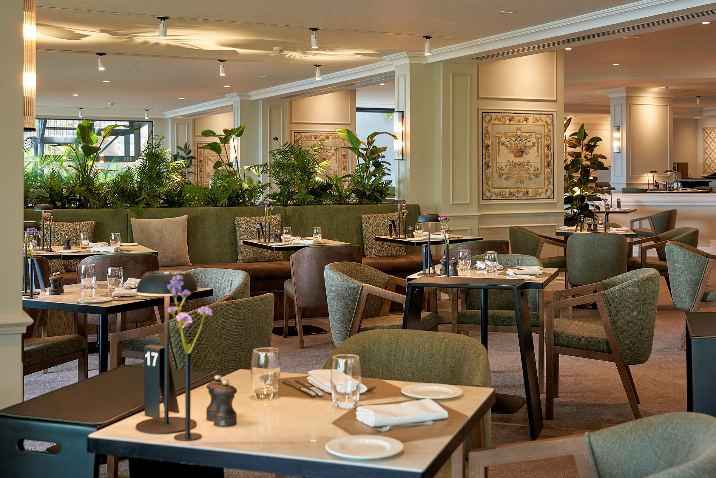 Et elegant restaurantområde med grønn innredning, bord dekket til måltider og dekorative plantearrangementer. (AI-generert tekst)