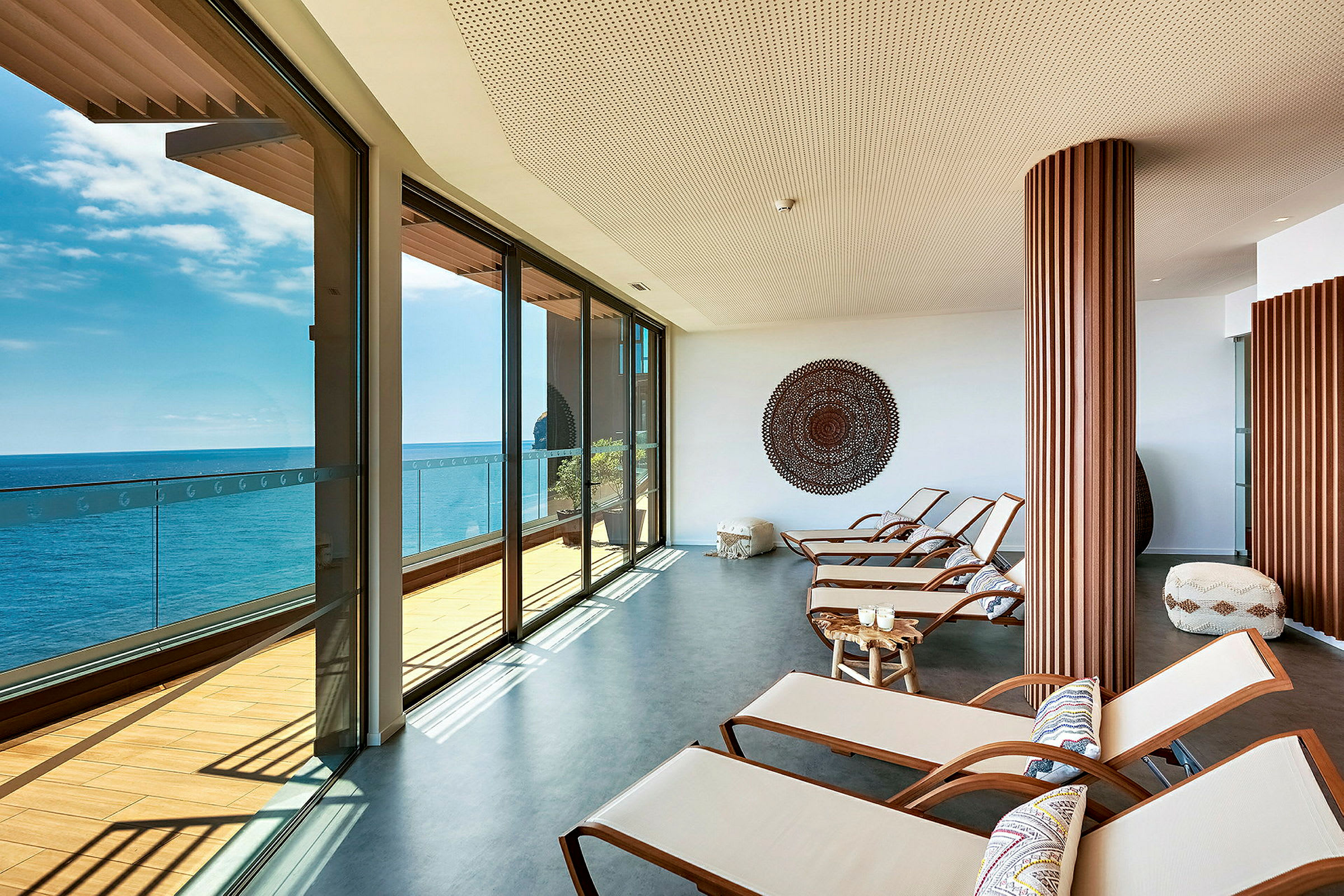 Utsikt over et lyst rom med solsenger og panoramavinduer mot havet. (AI-generert tekst)