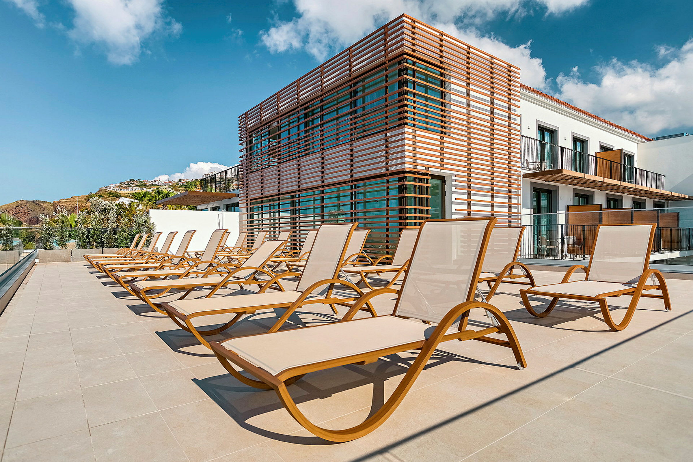Flere solsenger på en terrasse ved en moderne bygning. (AI-generert tekst)
