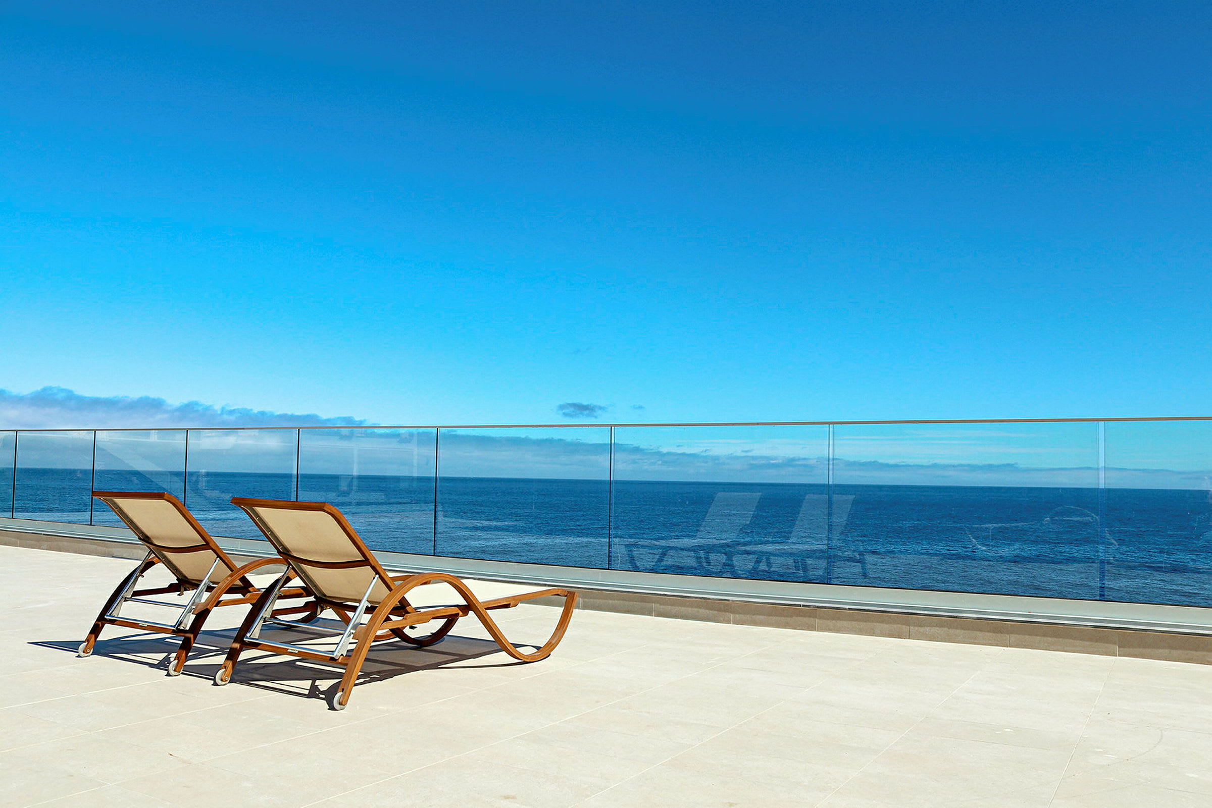 To solsenger på en terrasse med glassrekkverk og havutsikt. (AI-generert tekst)