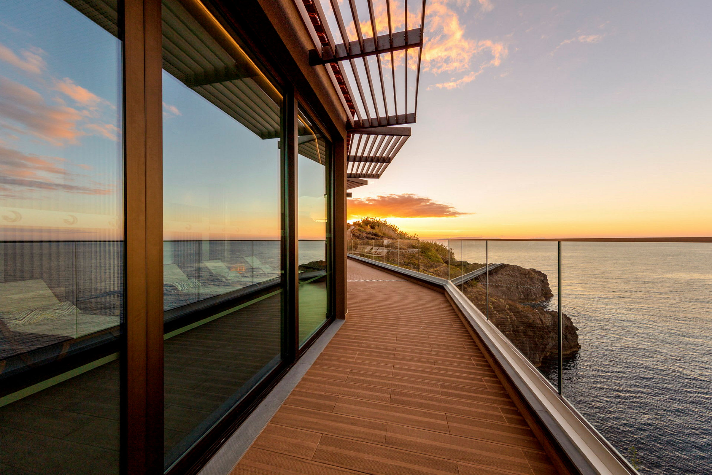 En terrasse med glassrekkverk og havutsikt, ved solnedgang. (AI-generert tekst)
