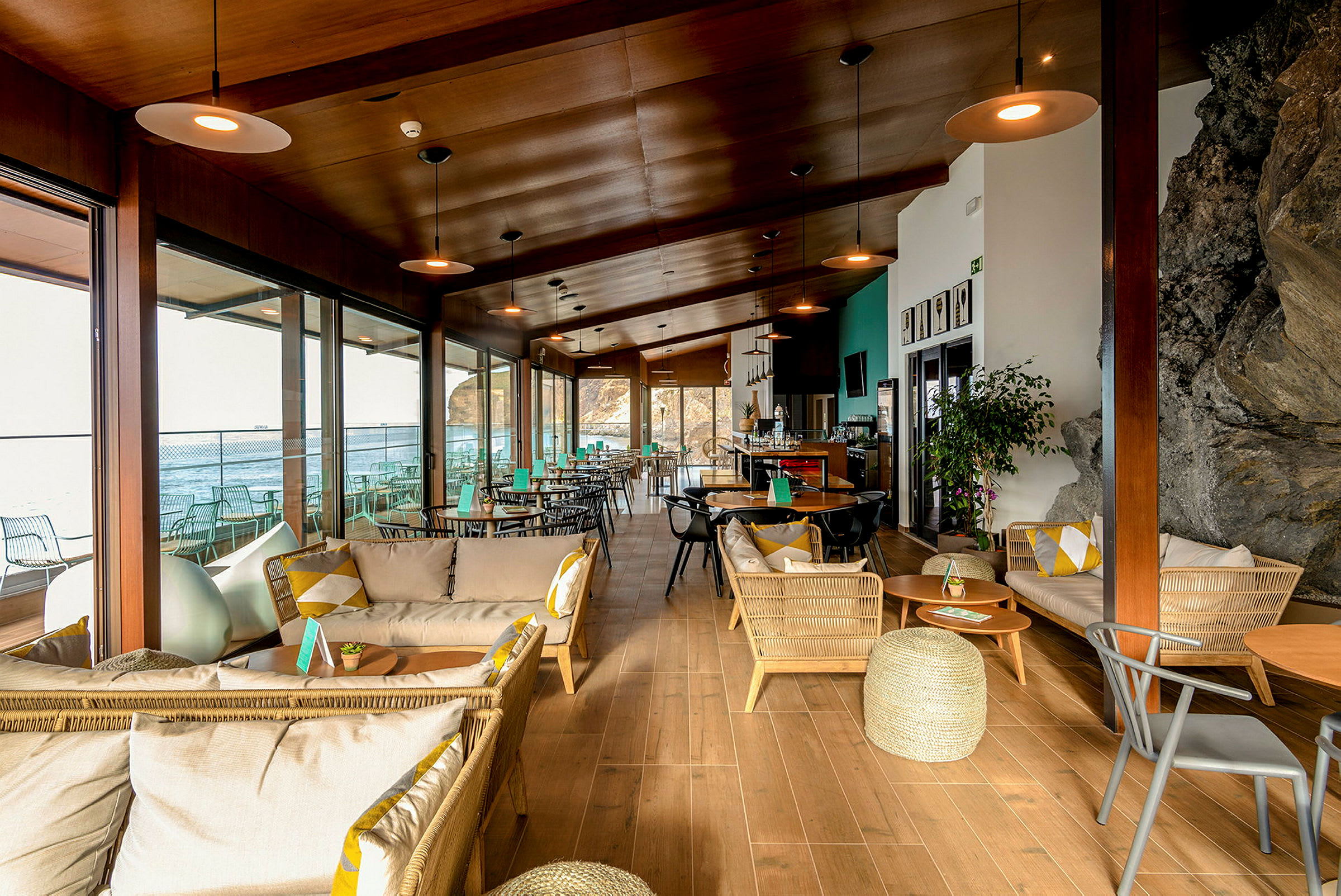Moderne kafé med treinnredning, sofaer og bord nær vinduer med utsikt mot havet. (AI-generert tekst)