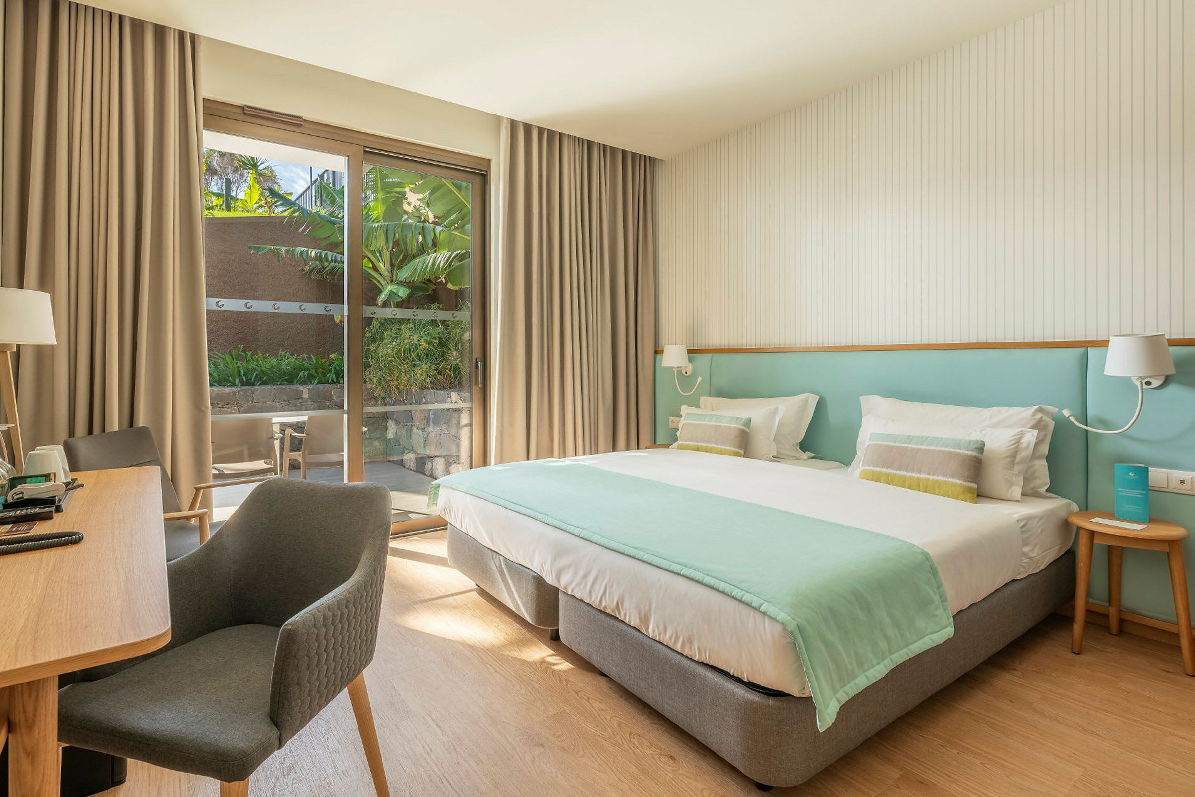 Hotellrom med dobbeltseng, skrivebord og sitteområde. Skyvedører fører ut til en privat terrasse. (AI-generert tekst)
