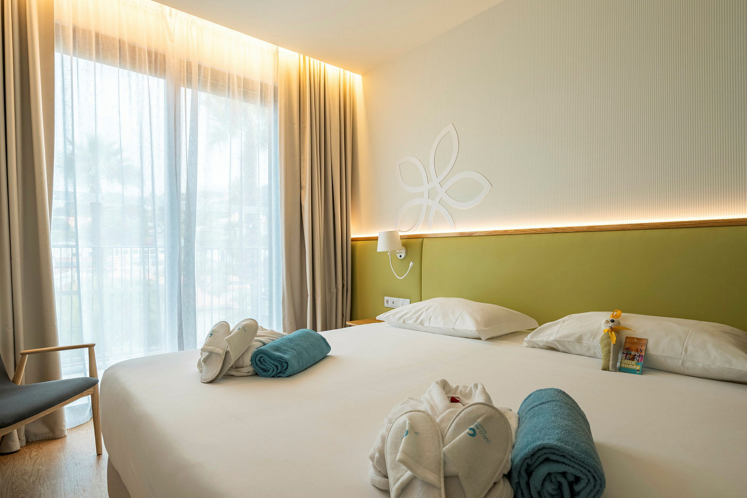 Hotellrom med en stor seng, lys innredning og et vindu med tynne gardiner. (AI-generert tekst)