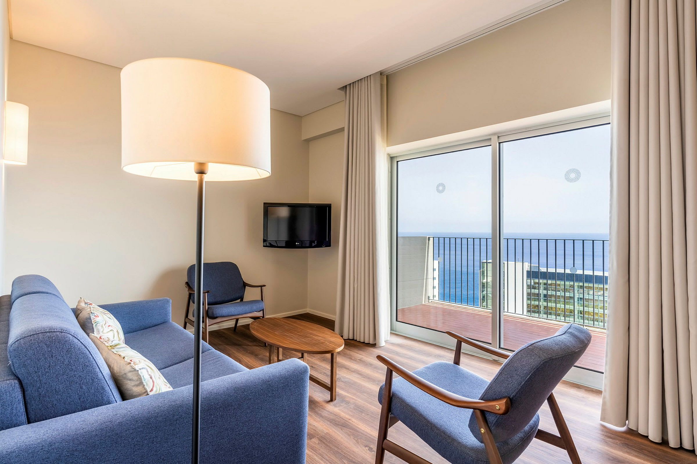 Stue med blå sofa og stoler, et trebord, og havutsikt gjennom en glassdør. (AI-generert tekst)