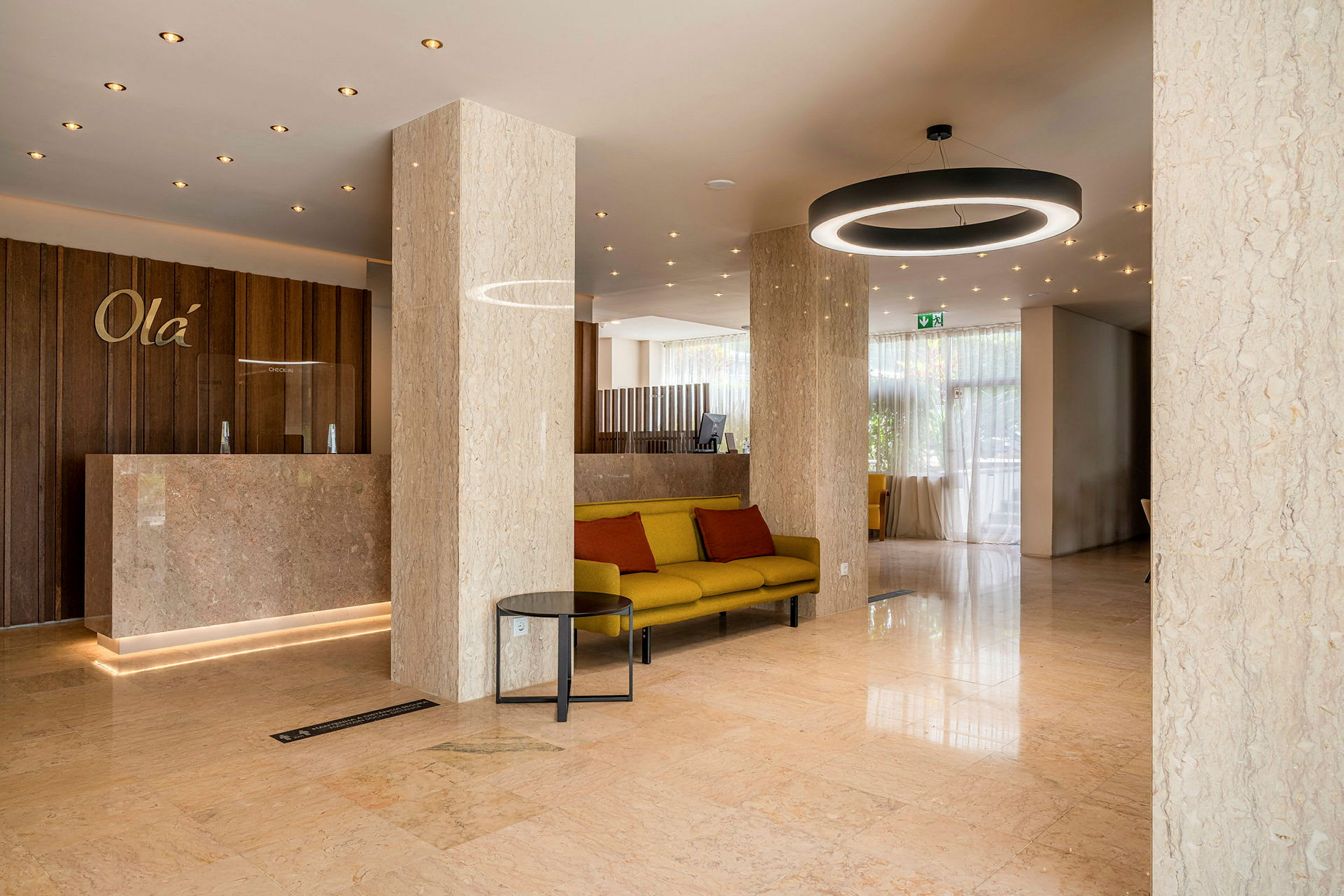 Hotellobby med marmorgulv og søyler, en resepsjon med panel av tre og en sittegruppe med gul sofa og røde puter. (AI-generert tekst)