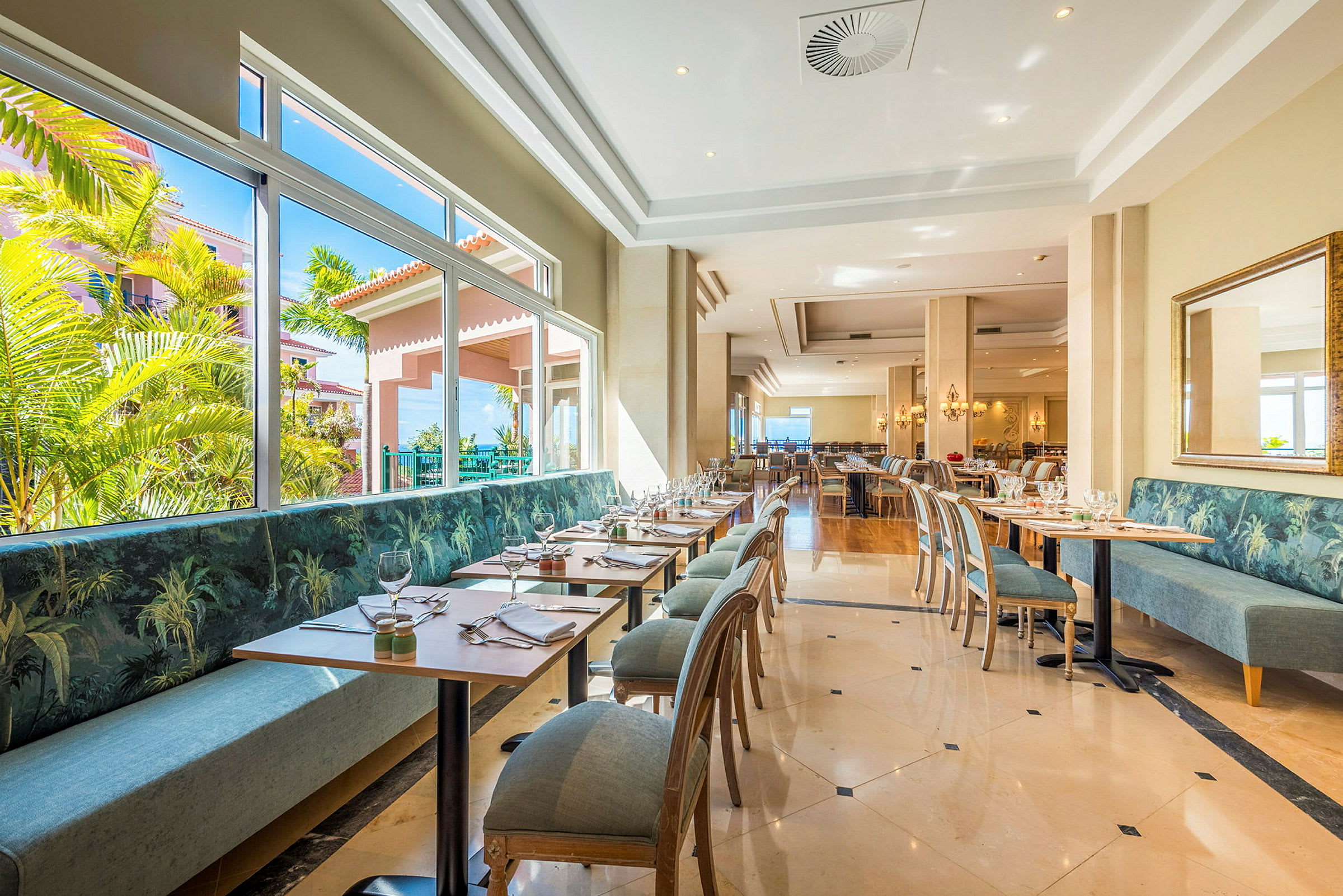 En lys restaurant med moderne bord og stoler samt store vinduer med utsikt over grøntområder. (AI-generert tekst)