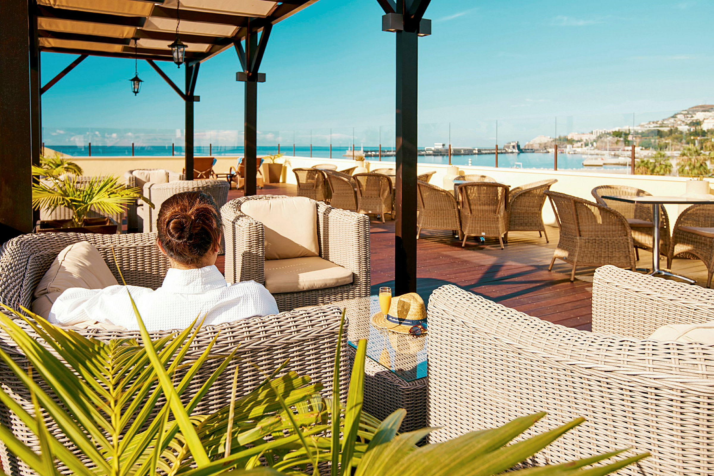 En person sitter i en flettet lenestol på en terrasse med utsikt over havet. (AI-generert tekst)
